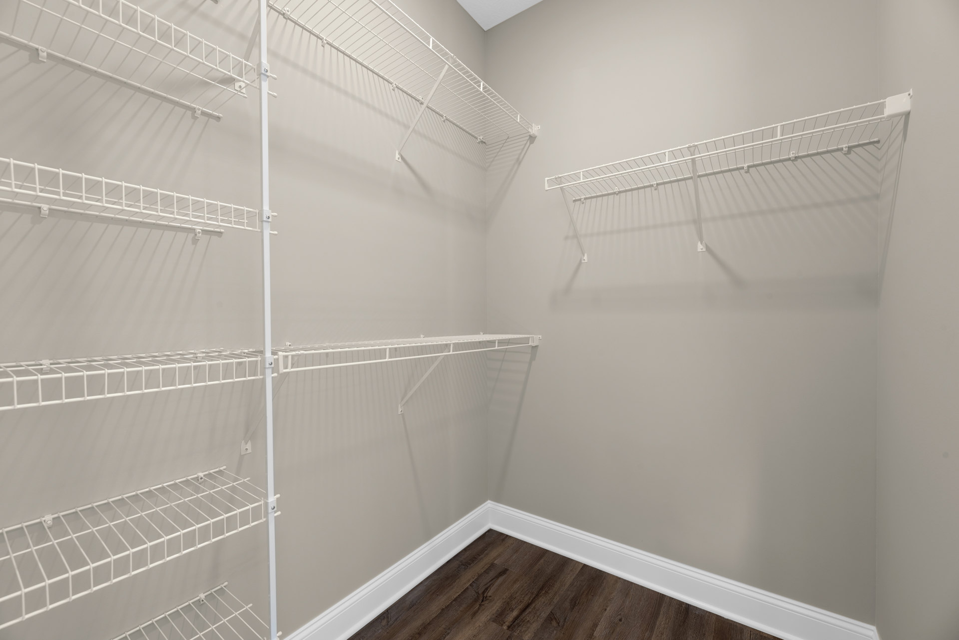 White wire shelves mounted on a white plaster wall above a wood floor, with a white clothes rack and white storage objects arranged neatly.