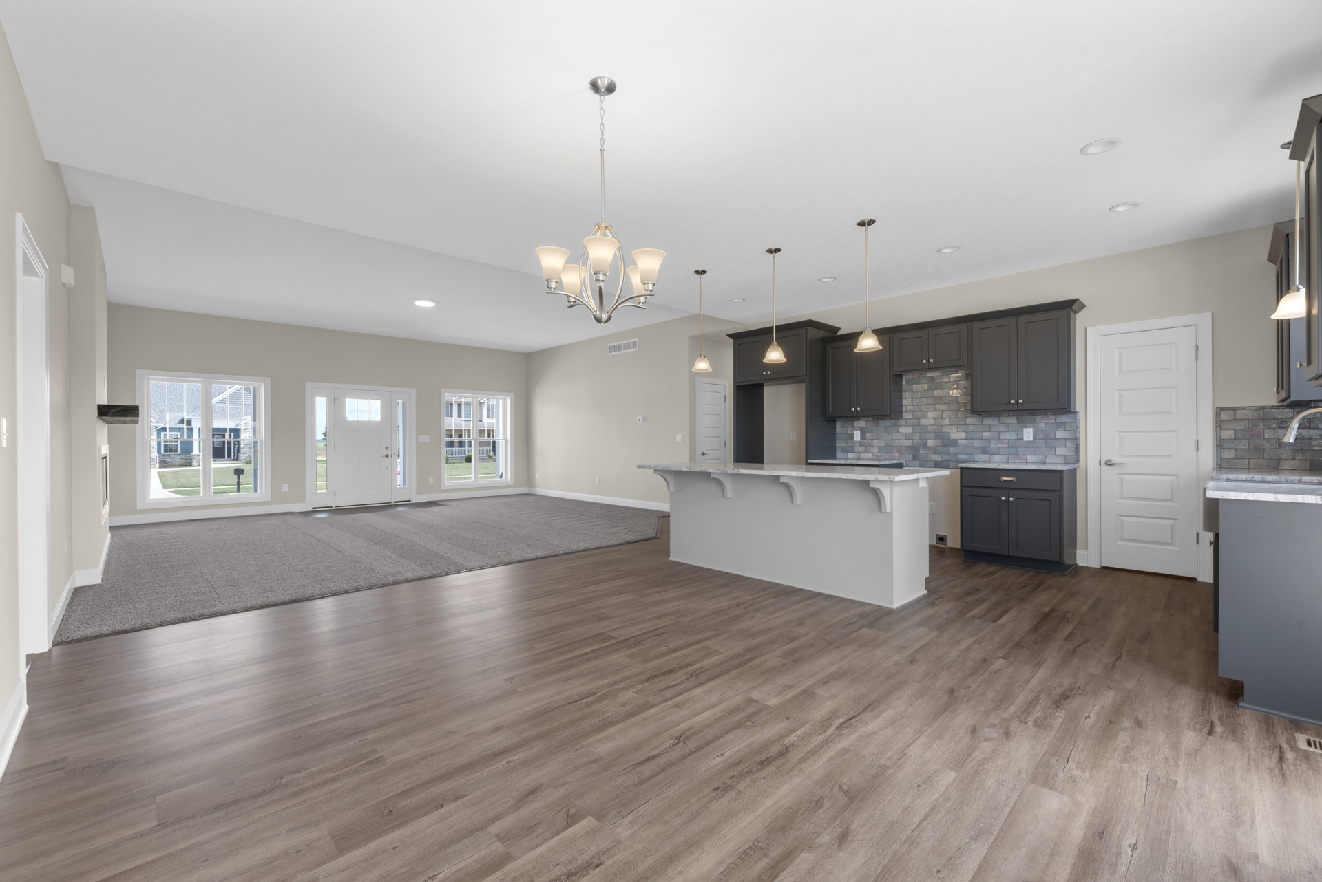 Open-concept kitchen and living room with white marble countertops, wood flooring, area rug, white cabinetry, stainless steel sink, and large window overlooking lawn and