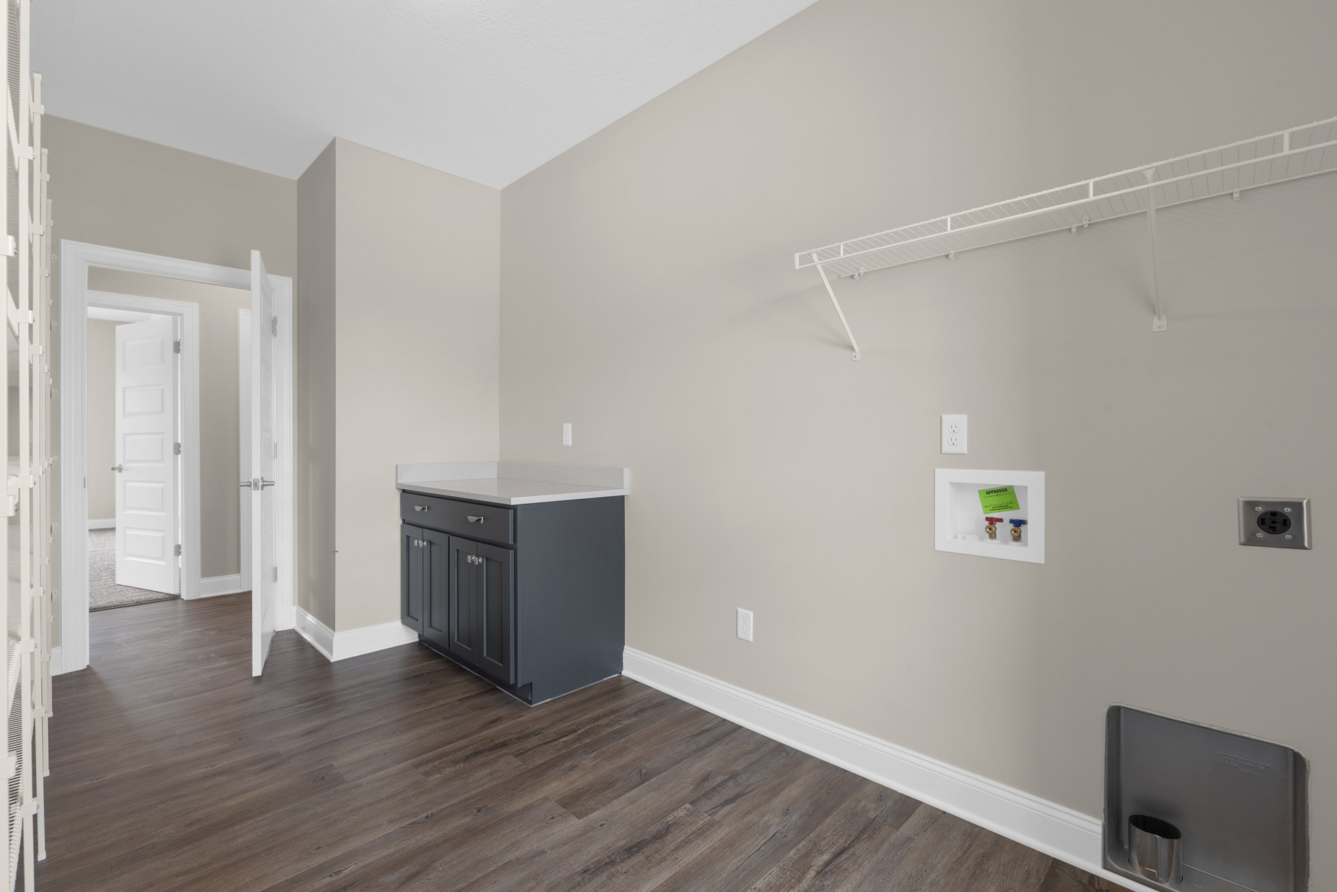 Open-concept room featuring a white floating shelf, black lower cabinets, white quartz countertop, laminate flooring, and plaster walls; includes a close-up of a power outlet and a