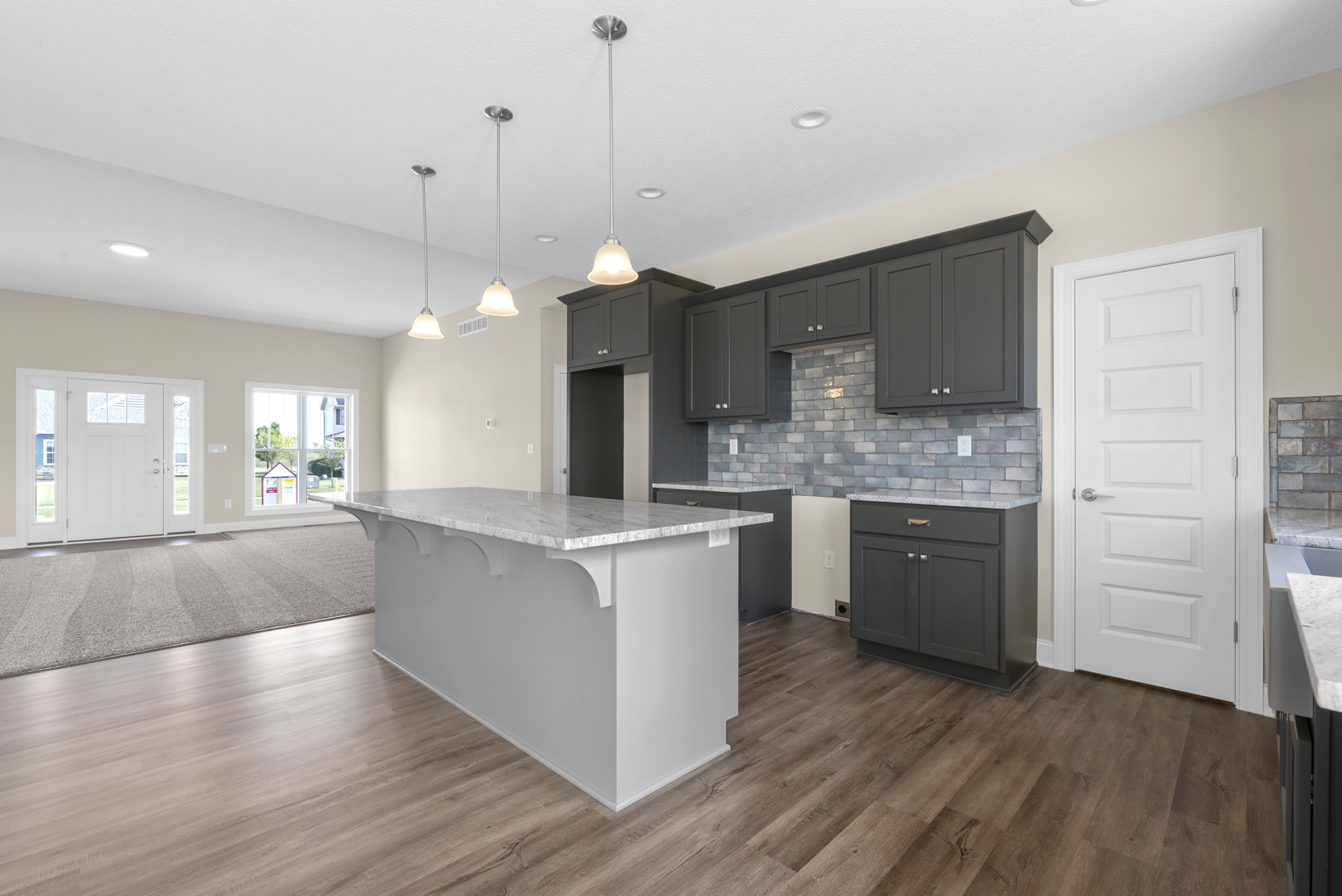 Open kitchen and dining area with wood flooring, white kitchen island topped with marble, grey cabinetry with marble counters, white walls, white doors with silver handles and