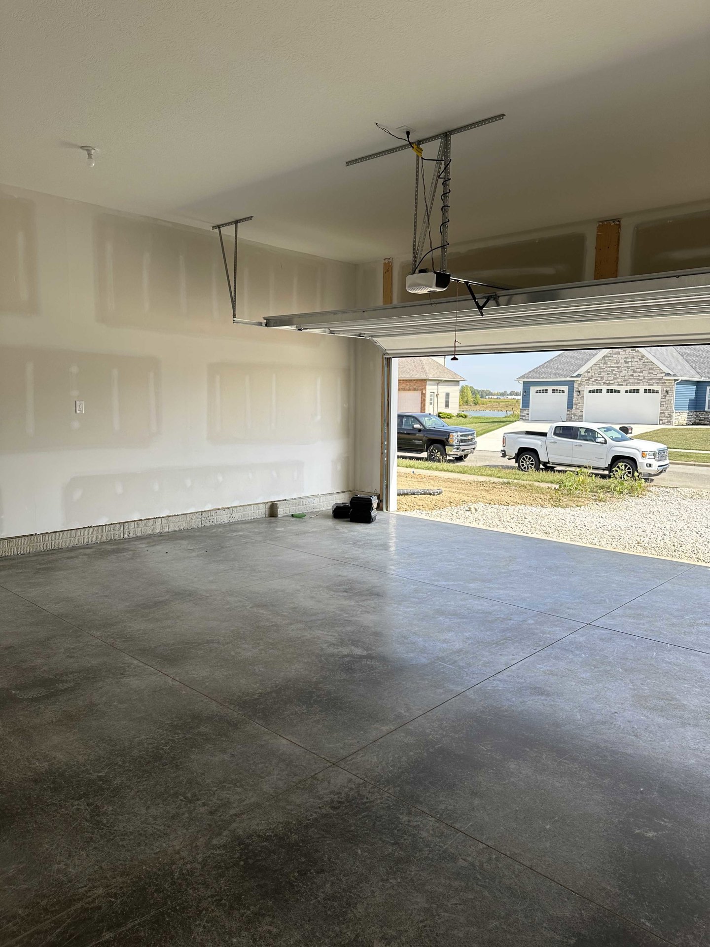 Garage with concrete floor, white plaster walls, two trucks parked in driveway, metal-framed electrical box, several black suitcases stacked near entrance.
