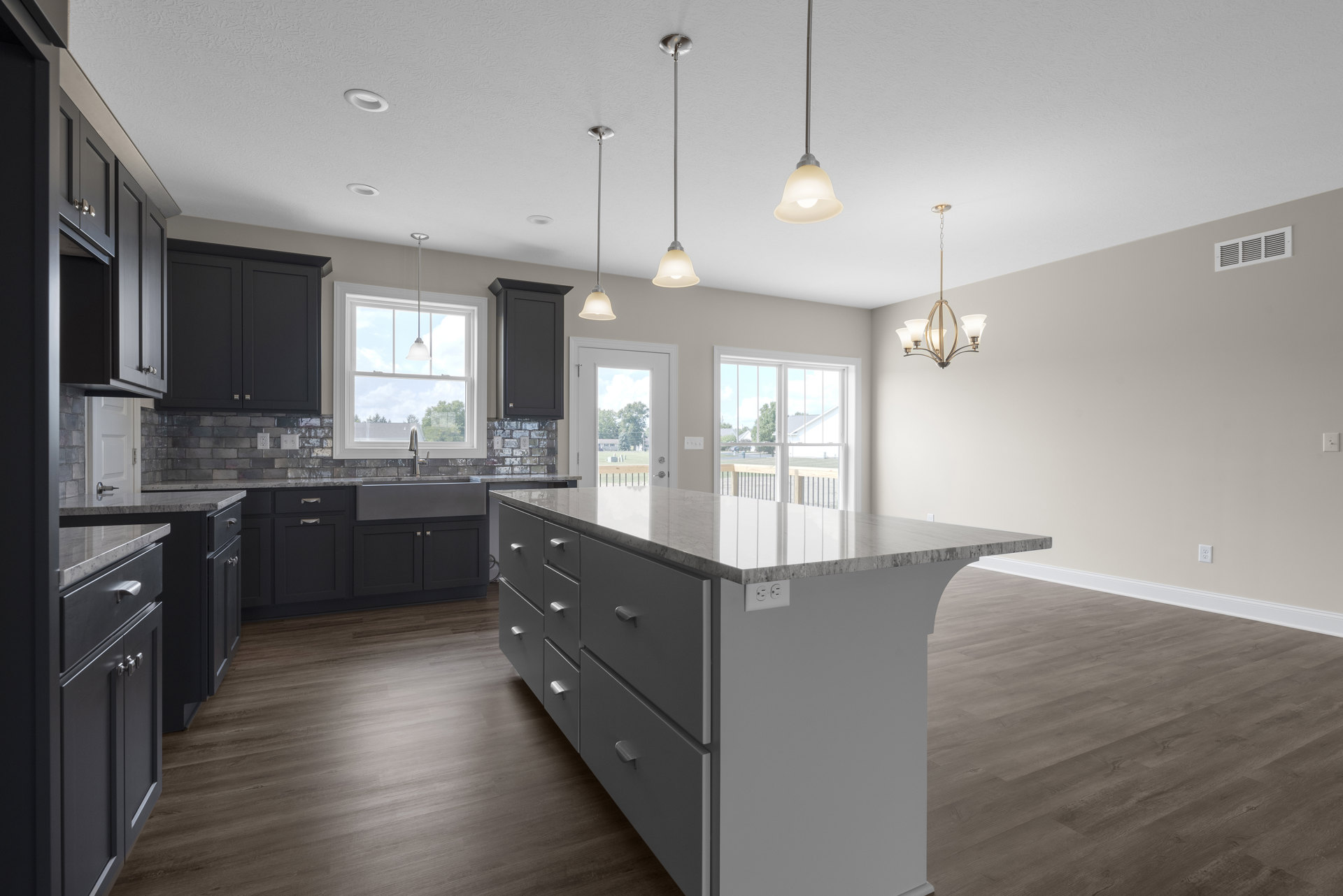 Spacious kitchen featuring a large central island with drawers, wood flooring, white cabinetry, stone countertops, stainless steel sink, and pendant lighting.