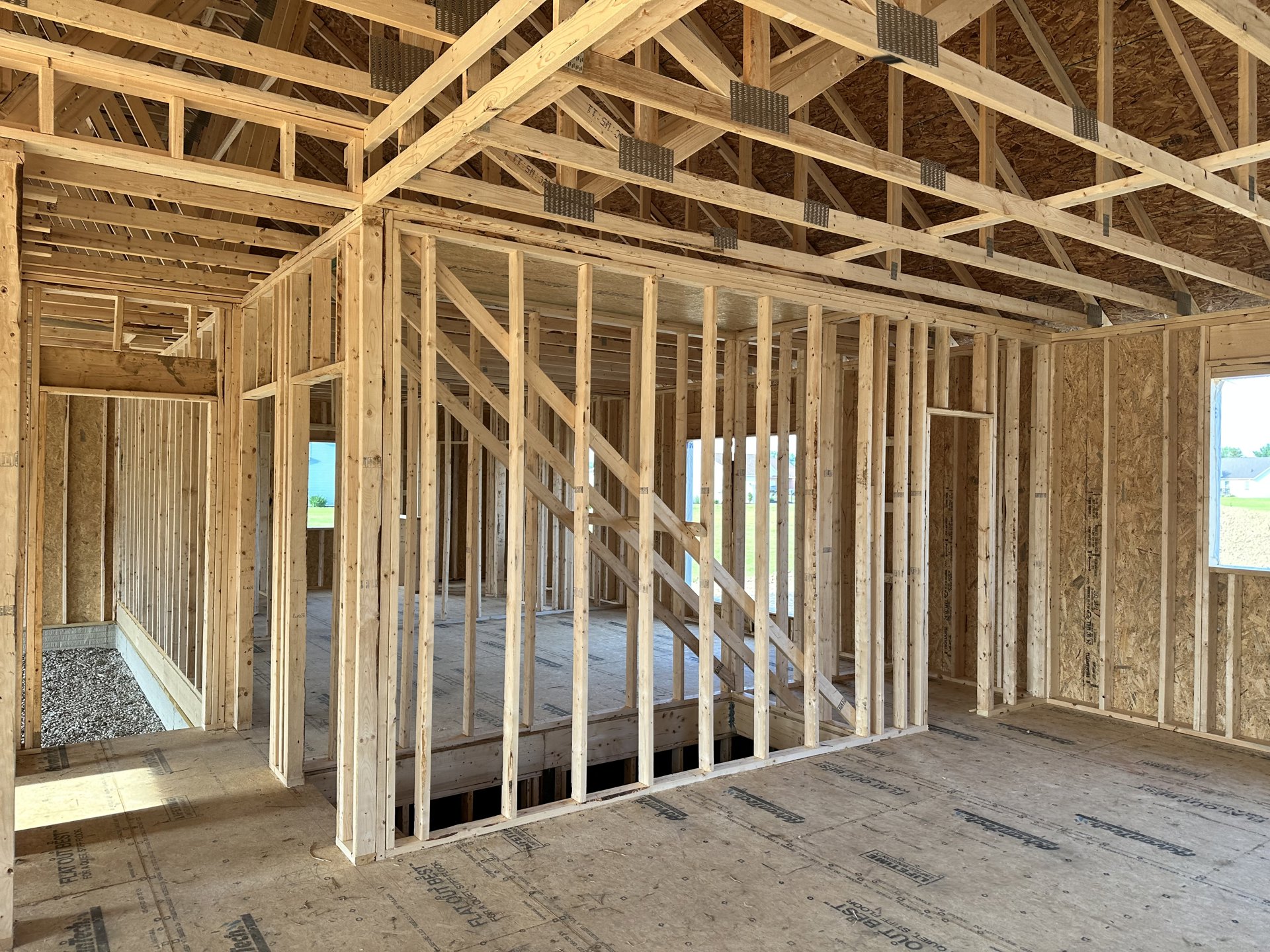 Exposed wooden framing and beams with metal studs, unfinished interior walls, window opening, pile of small rocks on ground, construction materials visible