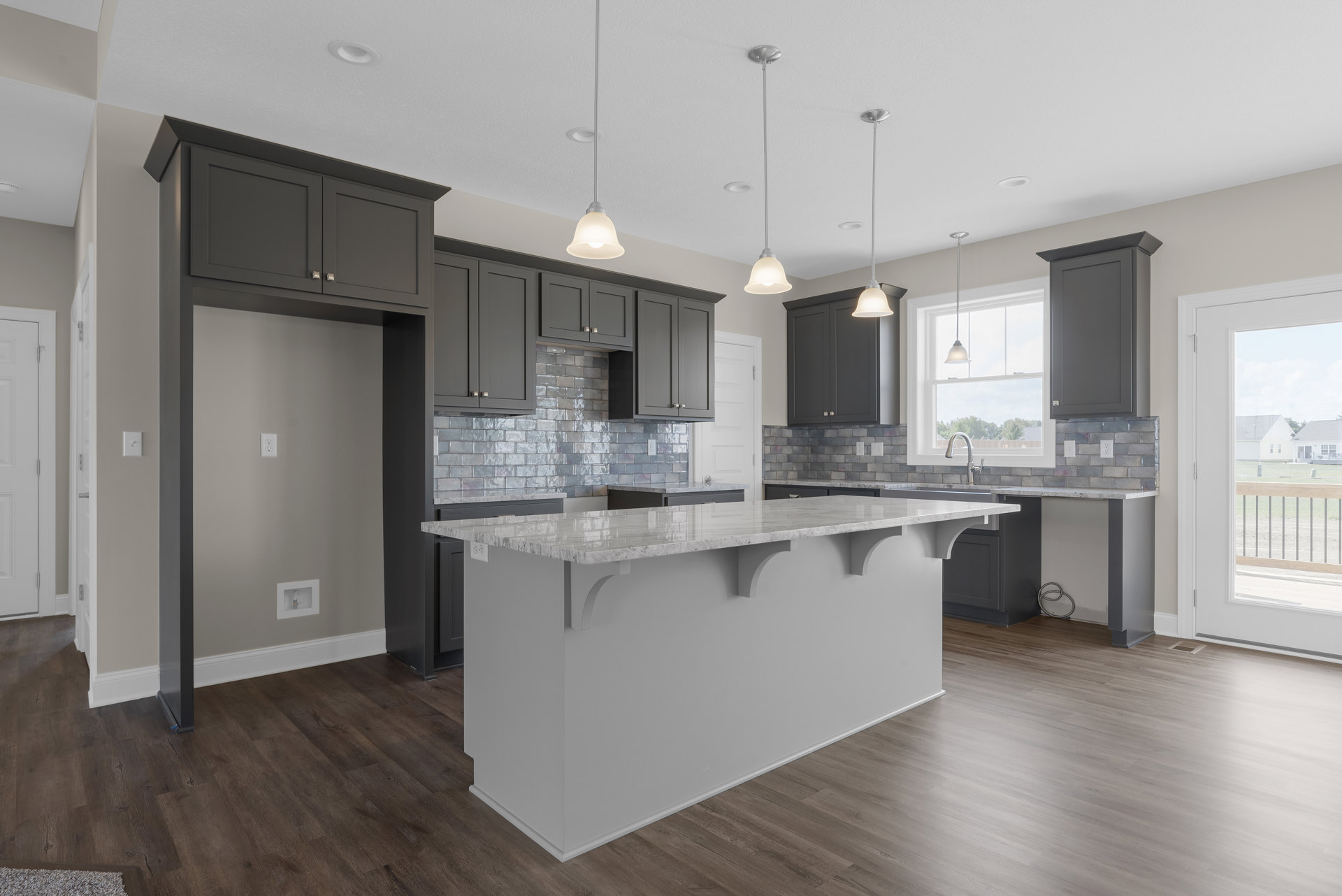 Open kitchen with white countertop bar, wood flooring, white cabinetry, stainless steel sink, bell-shaped pendant light, and hose mounted on wall.
