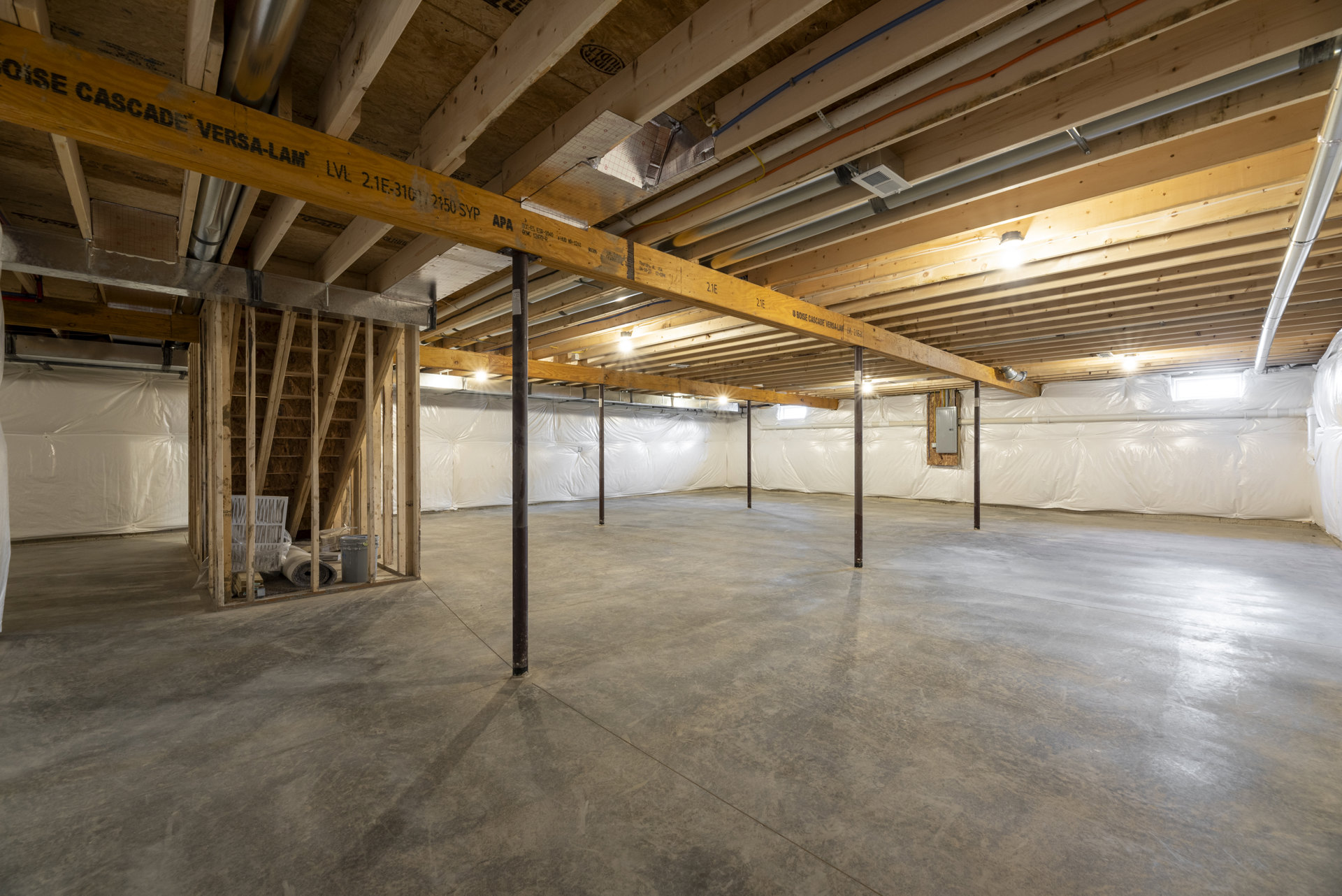 Open-concept room with exposed wooden ceiling beams, concrete floor, and visible steel support poles