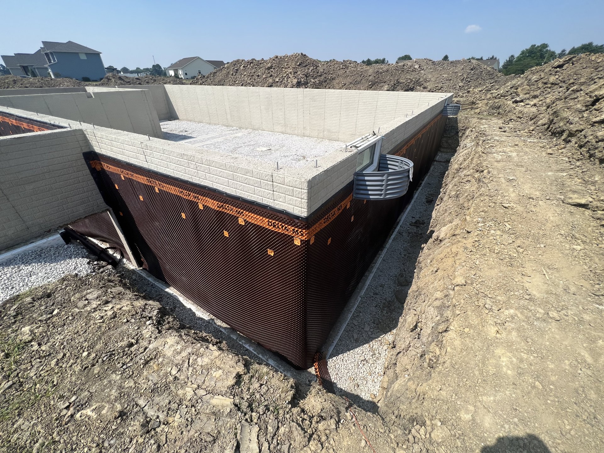 Concrete house foundation with exposed rebar, surrounded by dirt and rocks, plastic tub near a window opening, partially demolished structure, blue sky overhead