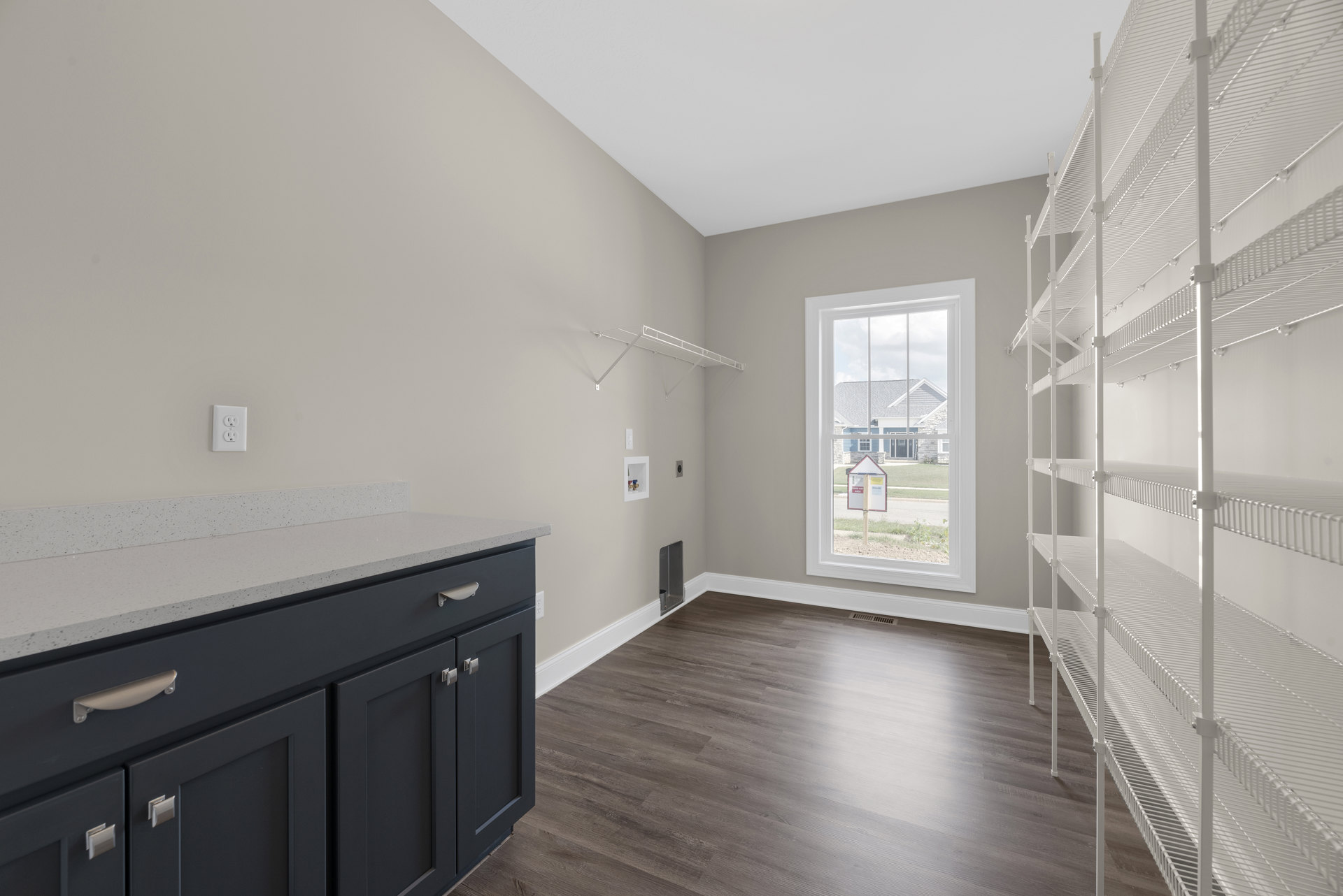 Kitchen with wood flooring, white cabinetry and drawers, open shelving, white countertop, window with a sign, and white electrical outlet on the wall