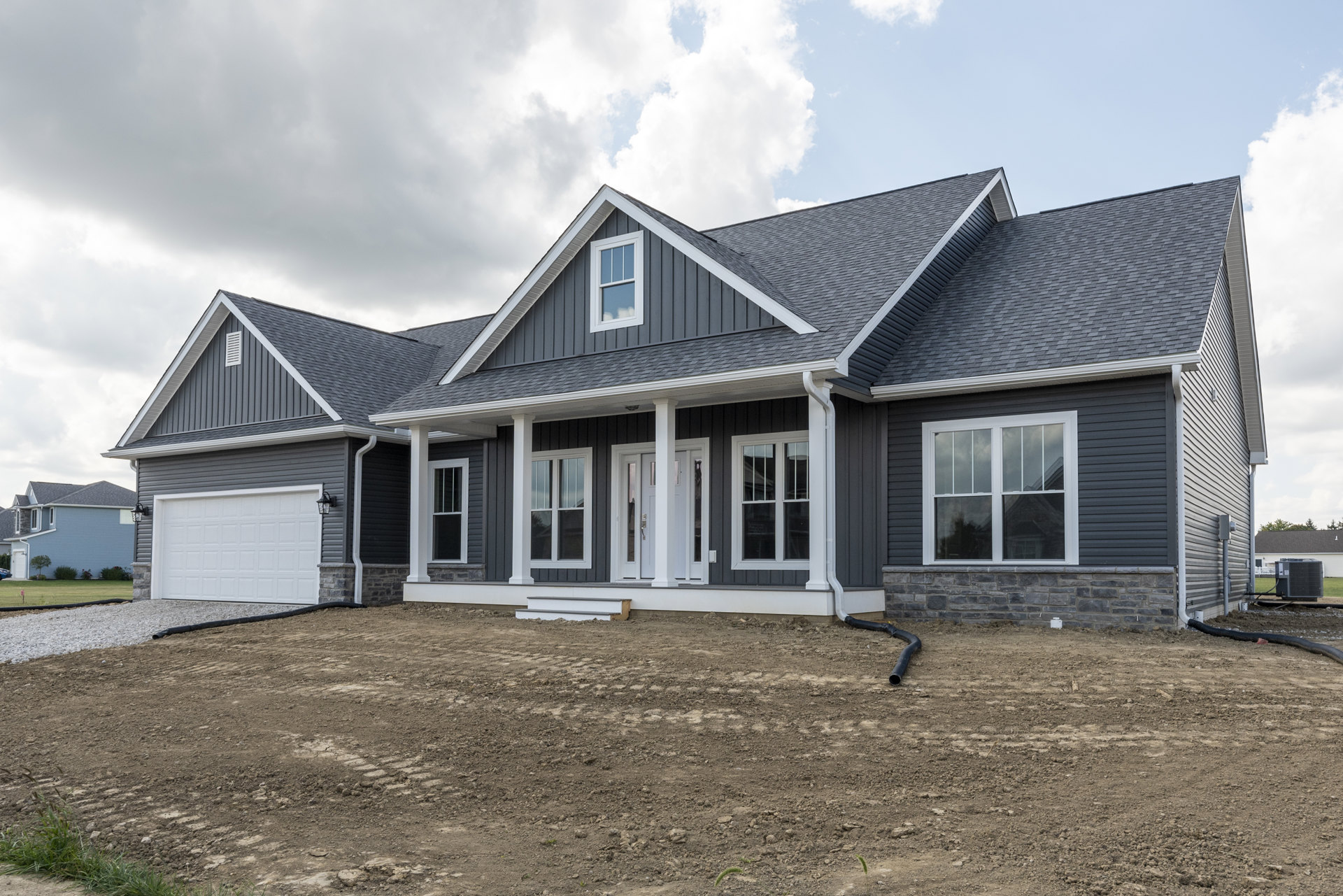 White single-story house with white-framed windows and door, set on a dirt yard under a cloudy sky, large grey HVAC unit with exposed wires near the building