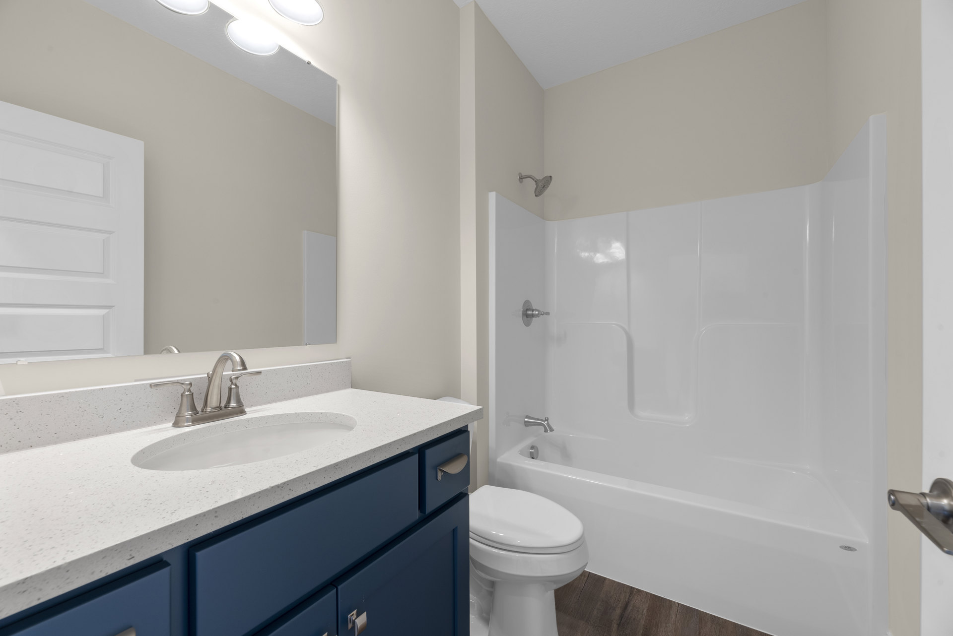 Bathroom with white bathtub, blue vanity cabinets, white sink, chrome faucet, closed white toilet, and tiled walls