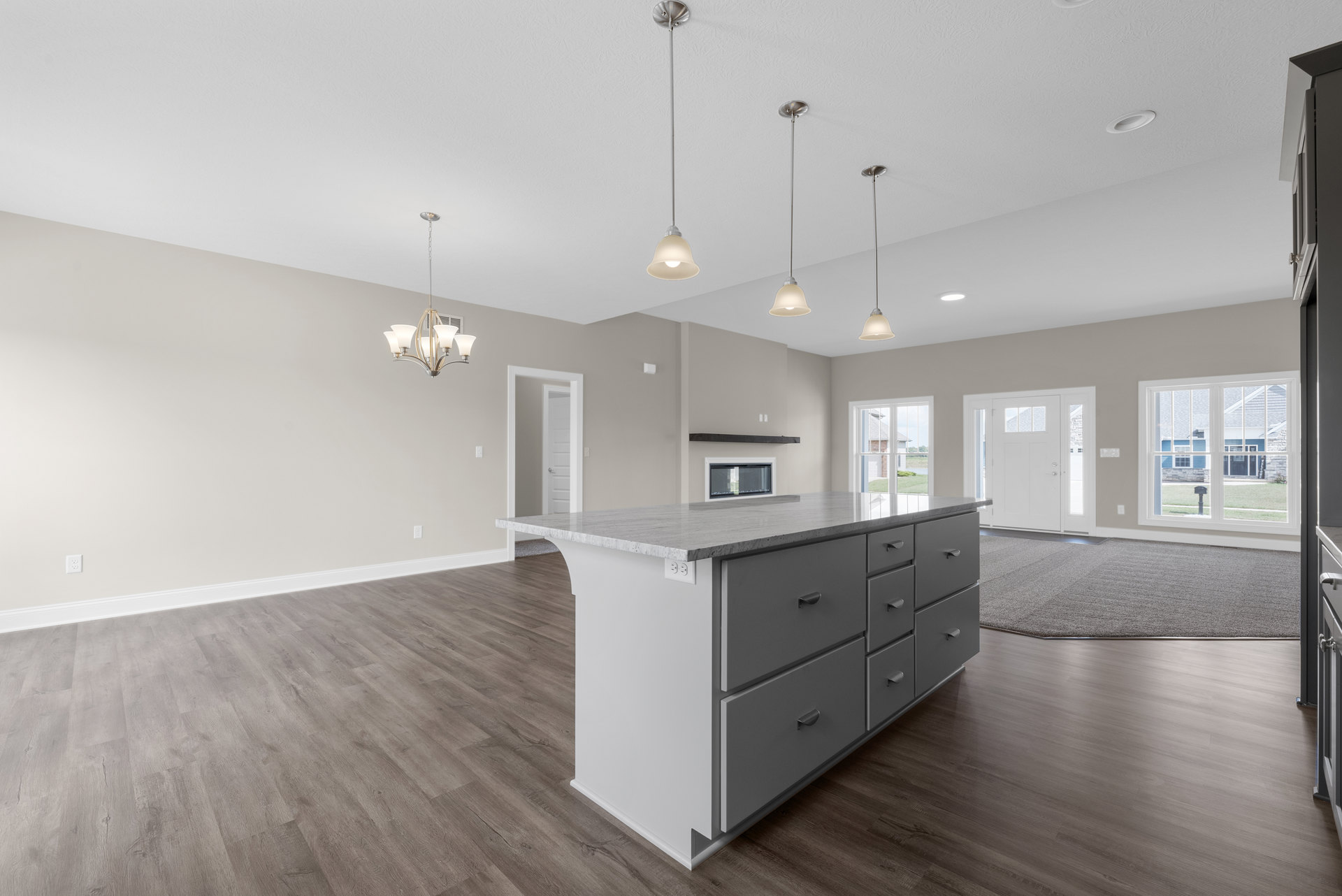 White kitchen with wood flooring, central island featuring drawers, white cabinetry, and a large window overlooking a green lawn and mailbox.