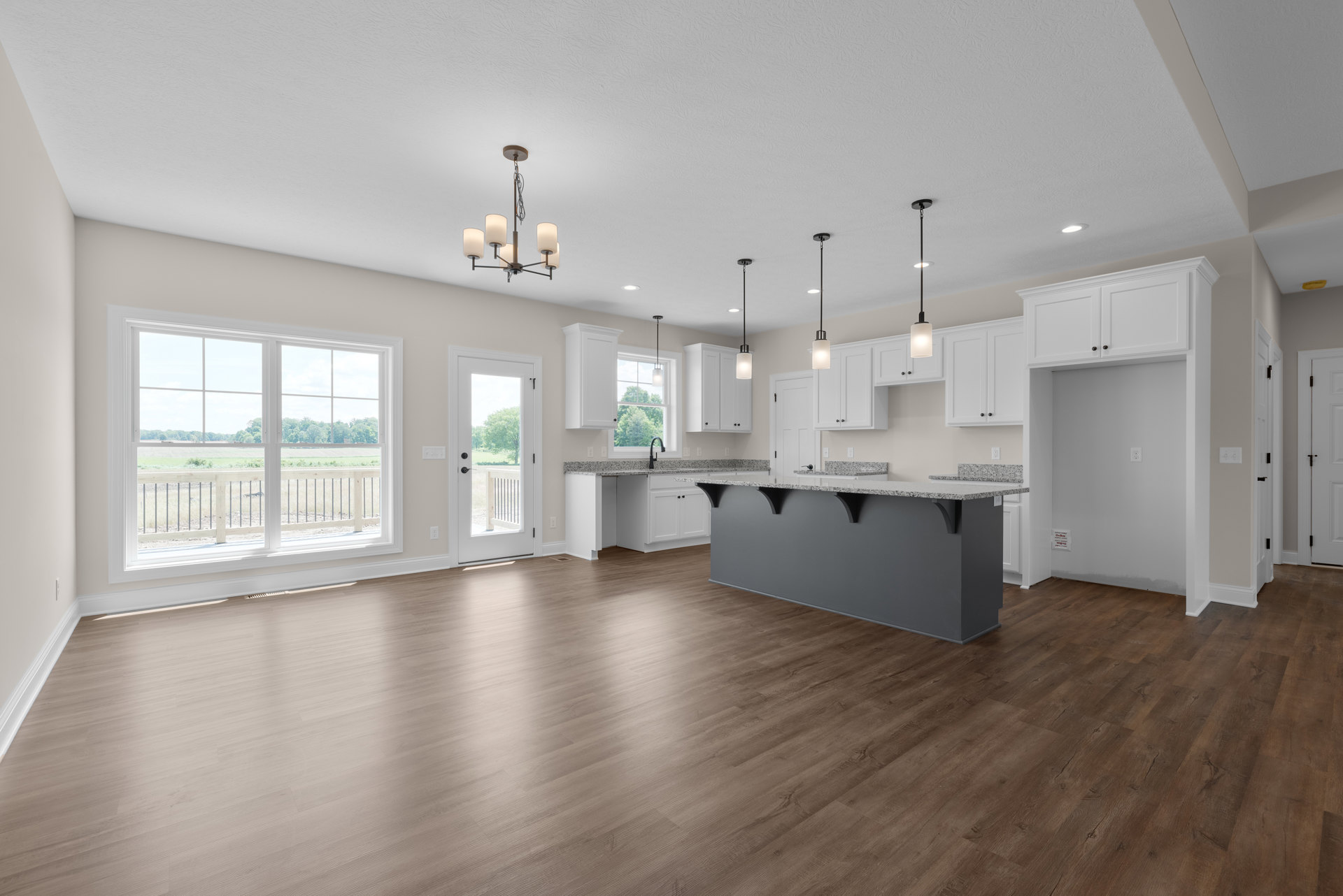 Spacious kitchen with marble-topped island, hardwood flooring, white cabinetry, large windows overlooking grassy yard, and modern pendant lamp