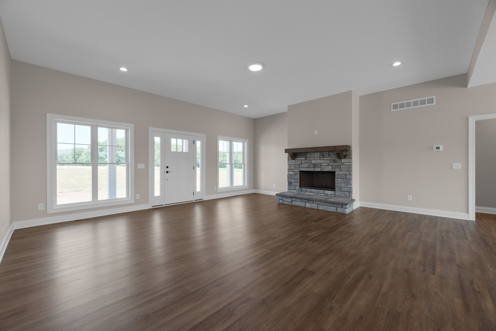 Living room with natural hardwood floors, white-framed windows, white door with glass panes, and stone fireplace surrounded by neutral walls.