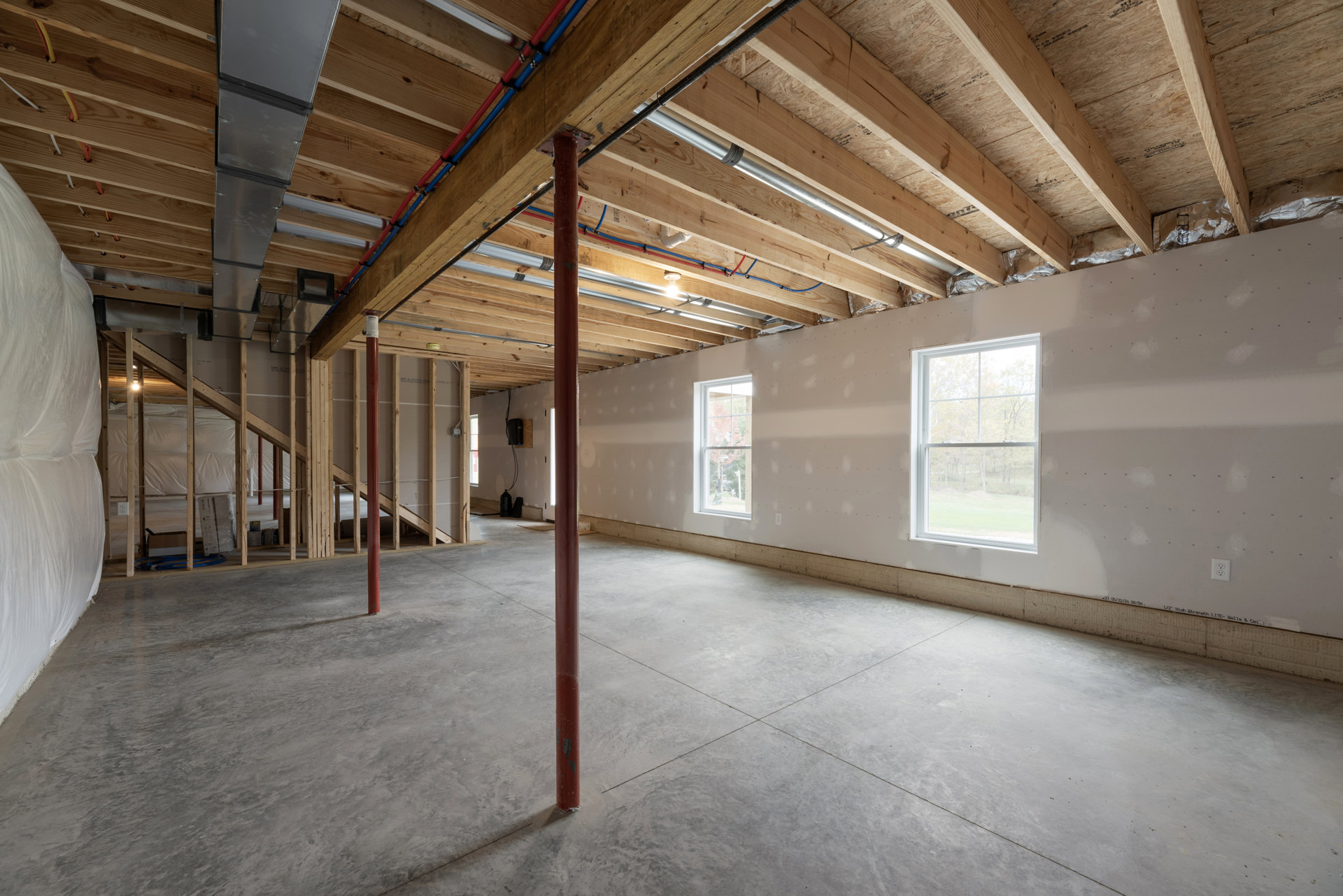 Concrete floor and wood ceiling in a room with exposed pipes, red support pole, and large window overlooking trees.