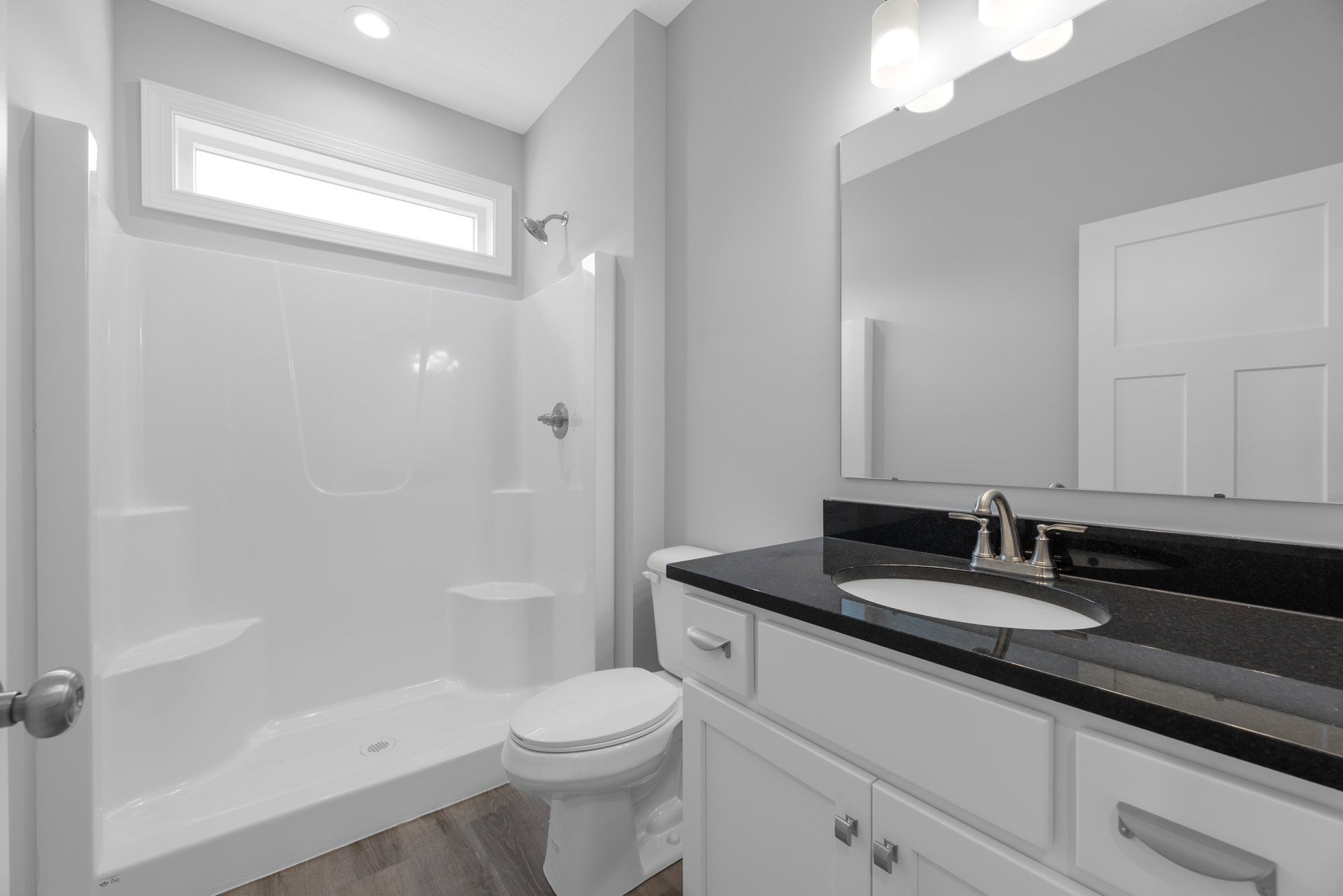 Bathroom with white toilet, black countertop sink, wall-mounted shower head, light gray tile walls, rectangular ceiling light, and white cabinetry