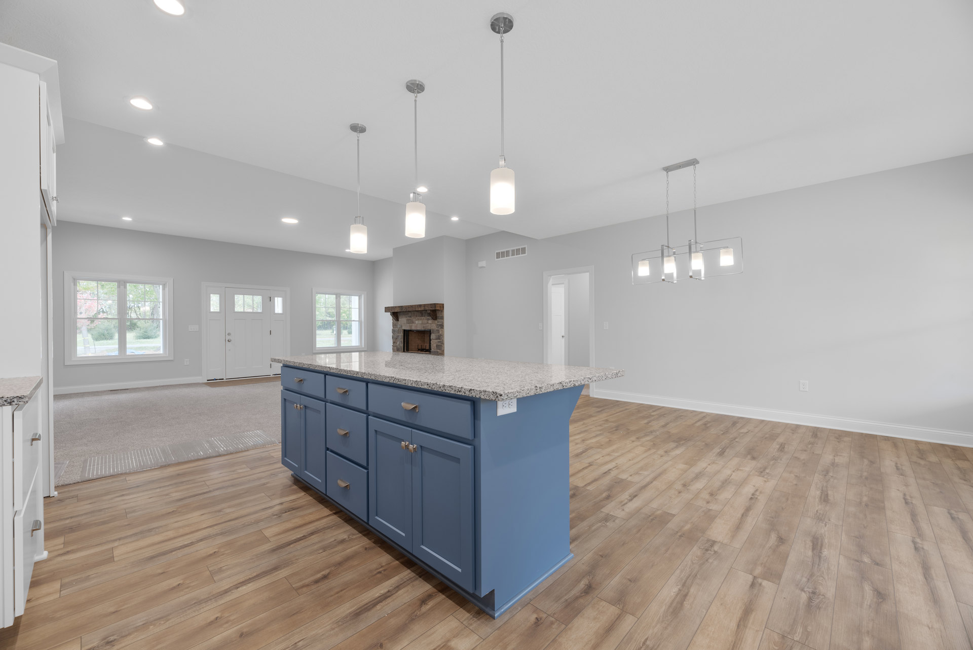 Granite kitchen island with white cabinetry, pendant lighting above, large window showing trees, hardwood flooring, white door with glass panes