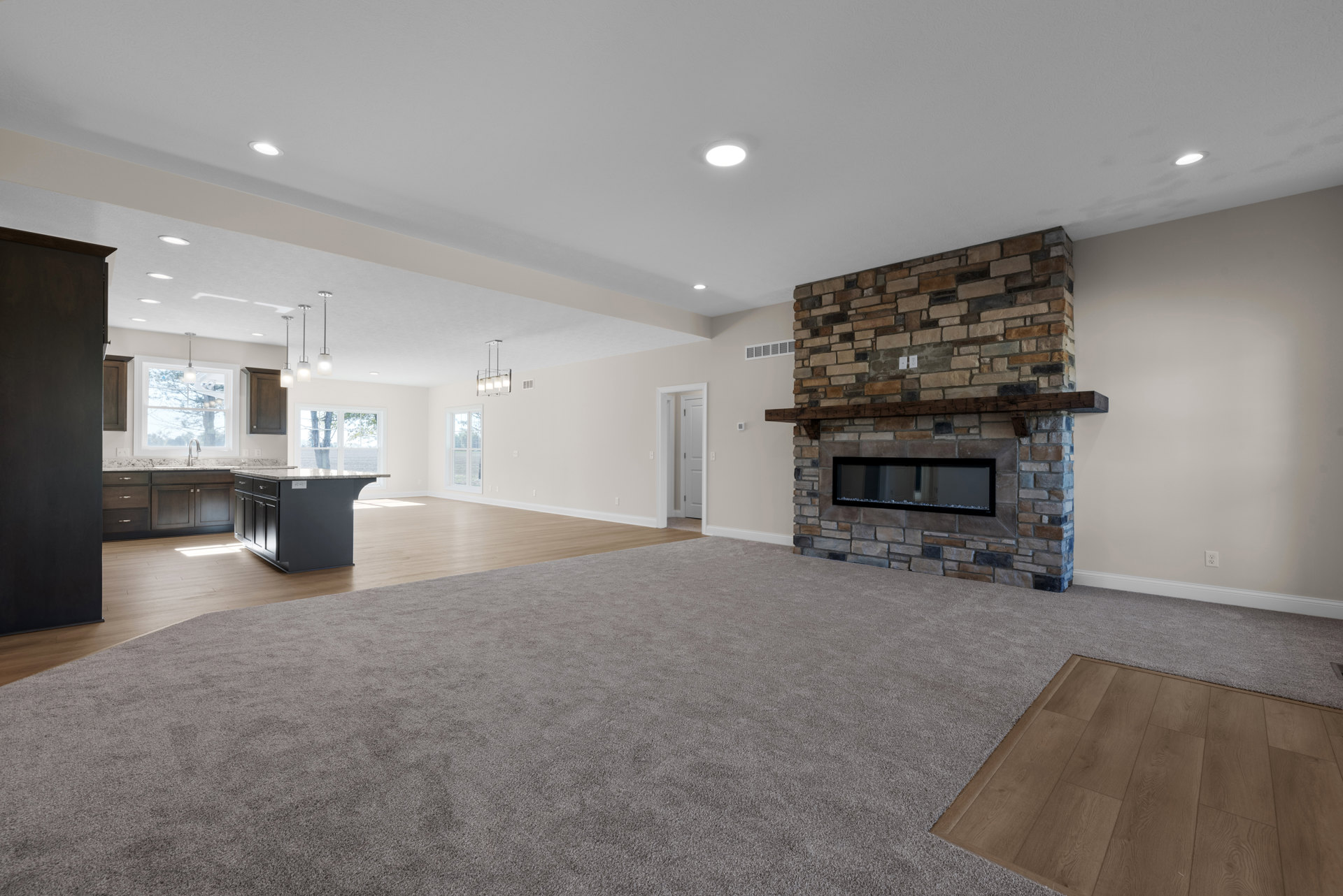 Open concept living room with wood flooring, marble kitchen island, modern fireplace featuring black surround and decorative rocks, white bordered accent wall, neutral carpet area