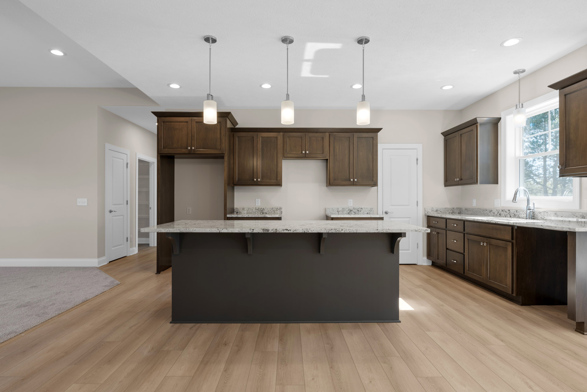 Spacious kitchen featuring a large central island with white countertop, dark accent wall, wood flooring, modern cabinetry, stainless steel faucet, and built-in appliances.