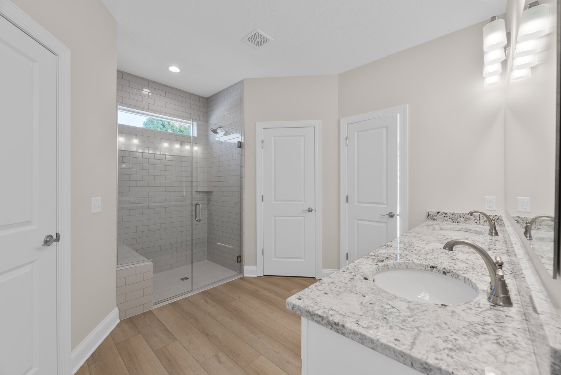 Marble bathroom countertop with undermount sink and chrome faucets, glass shower enclosure with white tile walls, white door with silver handle, light-colored cabinetry and