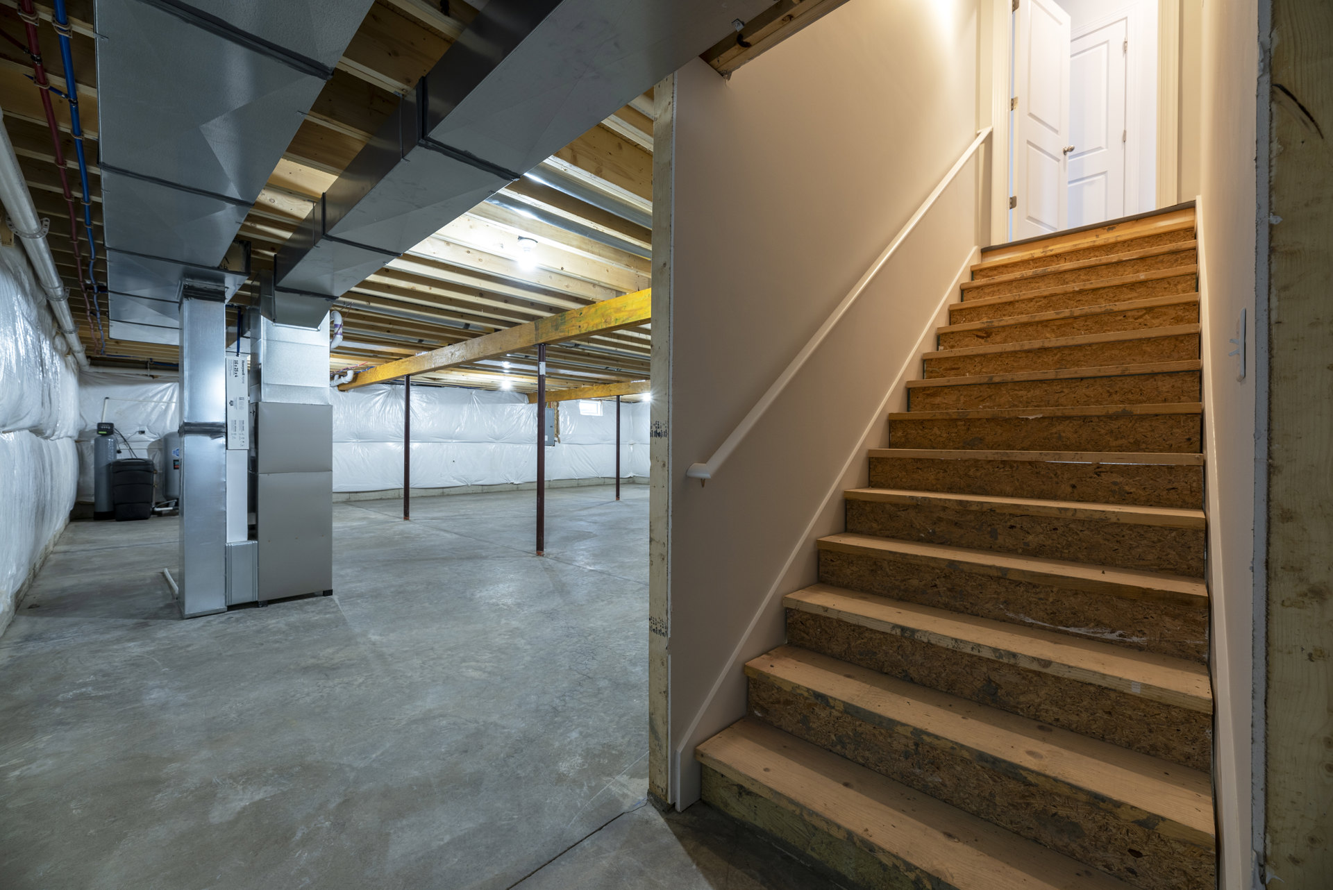 Wood staircase with metal handrail, exposed beams, composite wall finishes, and grey cylindrical fixture with green light in modern interior room