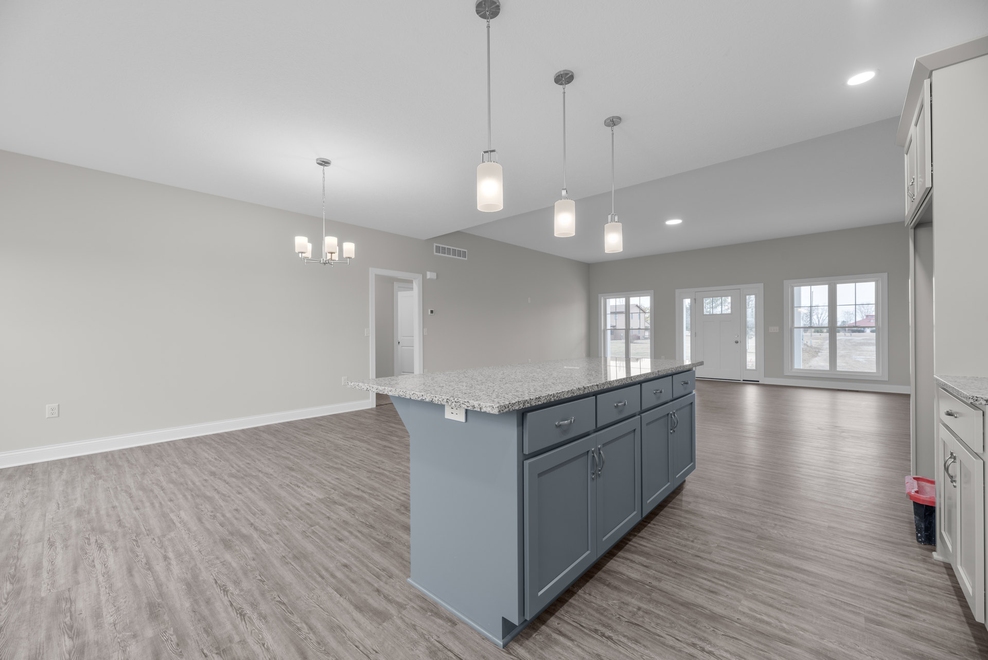 Granite kitchen island with undermount sink, stainless faucet, white cabinetry, pendant light fixture, window overlooking dirt road, hardwood flooring