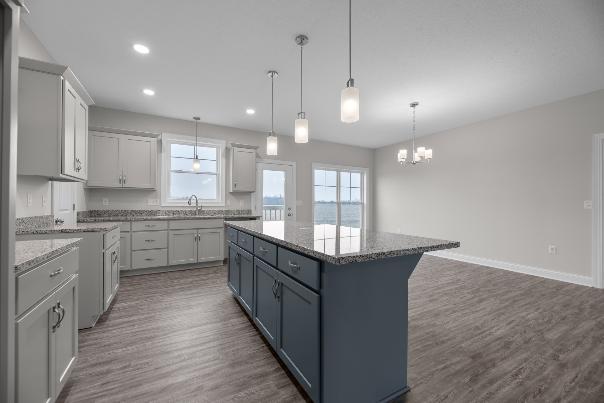Modern kitchen with marble-topped island, white cabinetry, stainless steel sink, pendant lighting, and hardwood flooring