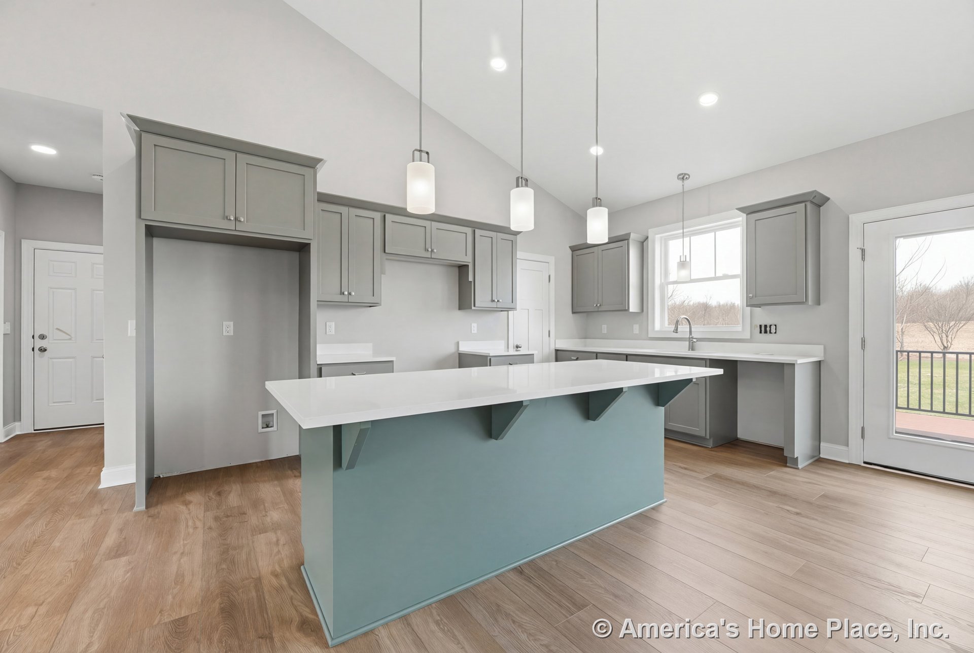 Light gray built-in cabinetry and a large blue island with white quartz countertops beneath a vaulted ceiling with recessed and pendant lighting; wood-look plank flooring, window