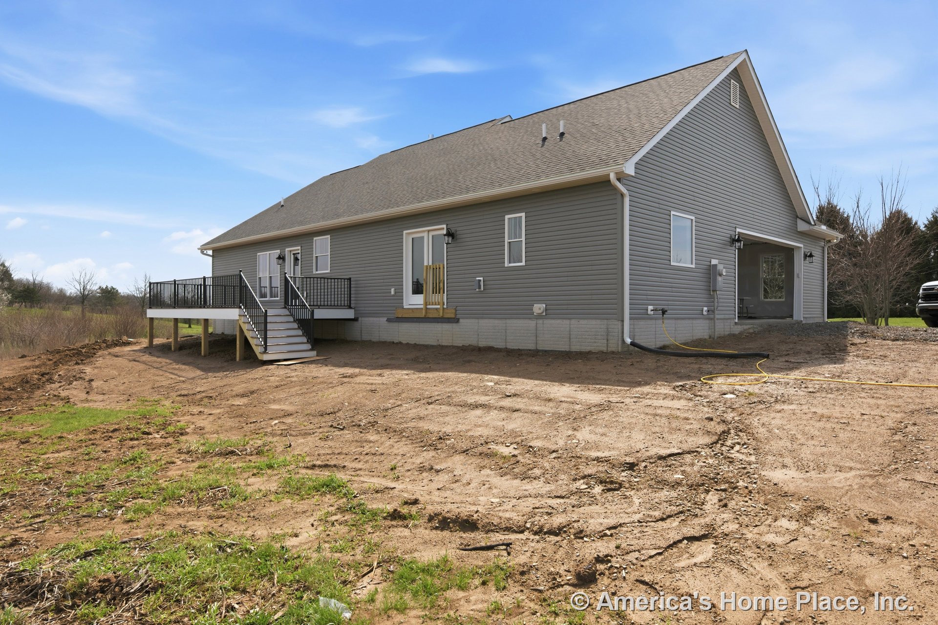 Gray vinyl siding exterior with white window trim, raised deck featuring black railings and stairs, sloped shingle roof, concrete foundation, sliding glass door, and outdoor