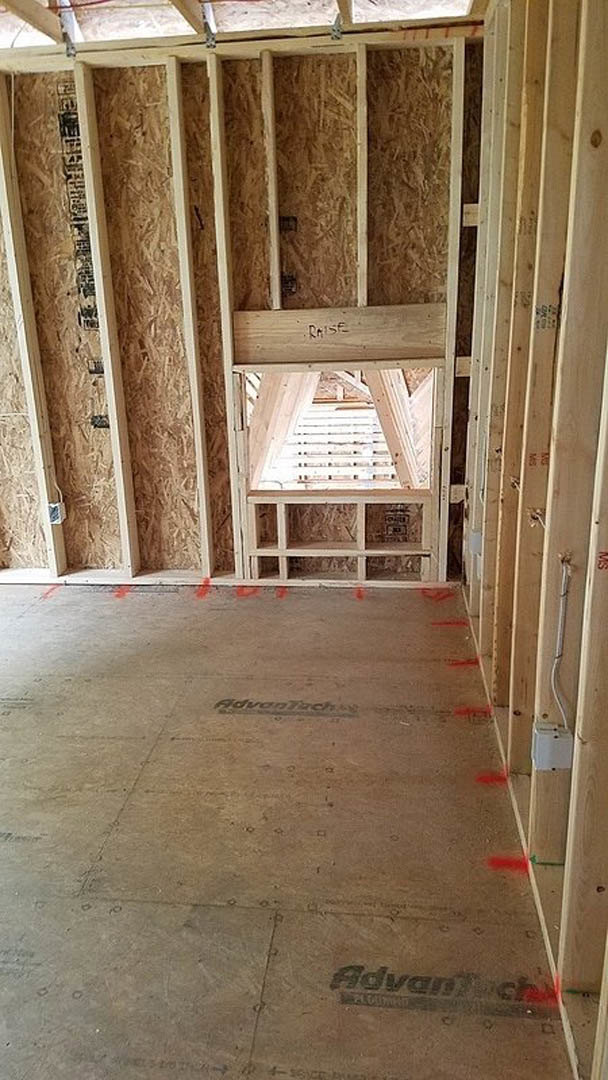 Wood-framed room under construction with exposed beams, ceiling insulation, window opening, and subfloor marked with red lines