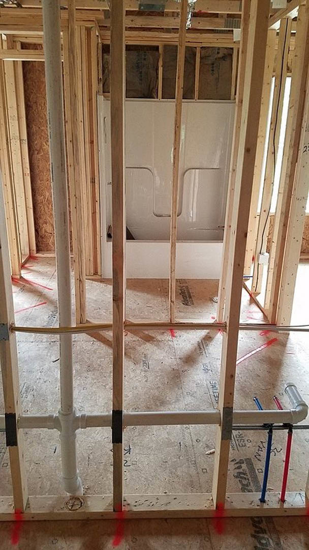 Bathroom under construction with exposed plumbing pipes, unfinished wood framing, insulation, and construction materials including a ladder and plaster.