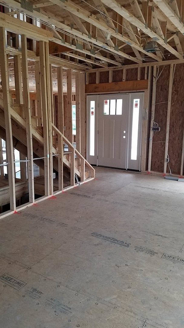 Unfinished staircase with exposed wooden framing, white door with glass panes, construction materials and insulation visible throughout interior