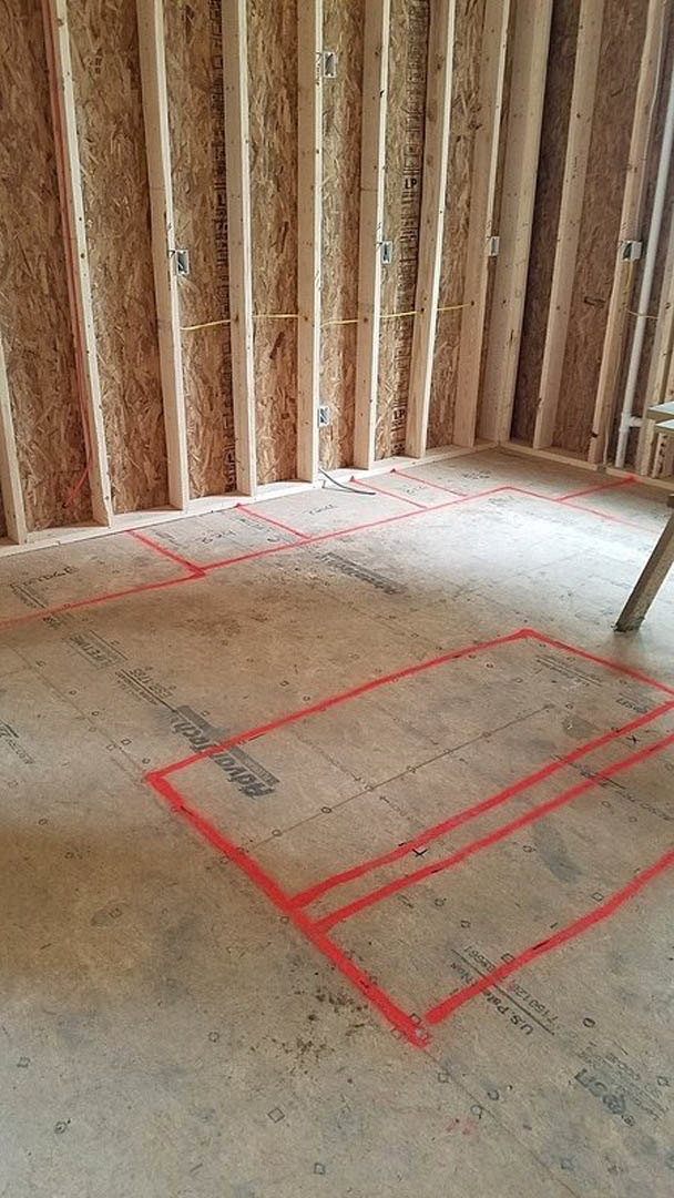 Wood-framed room under construction with red lines marked on concrete floor and cardboard surfaces, metal bar visible in foreground