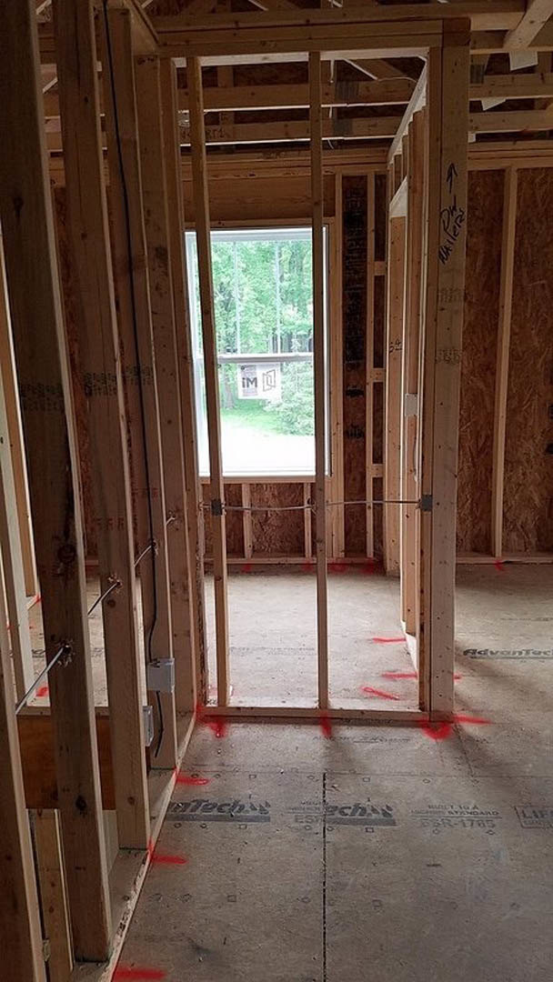 Sunlit room featuring a large window with a wood frame, exposed ceiling beams, concrete floor, and partially finished walls with visible insulation
