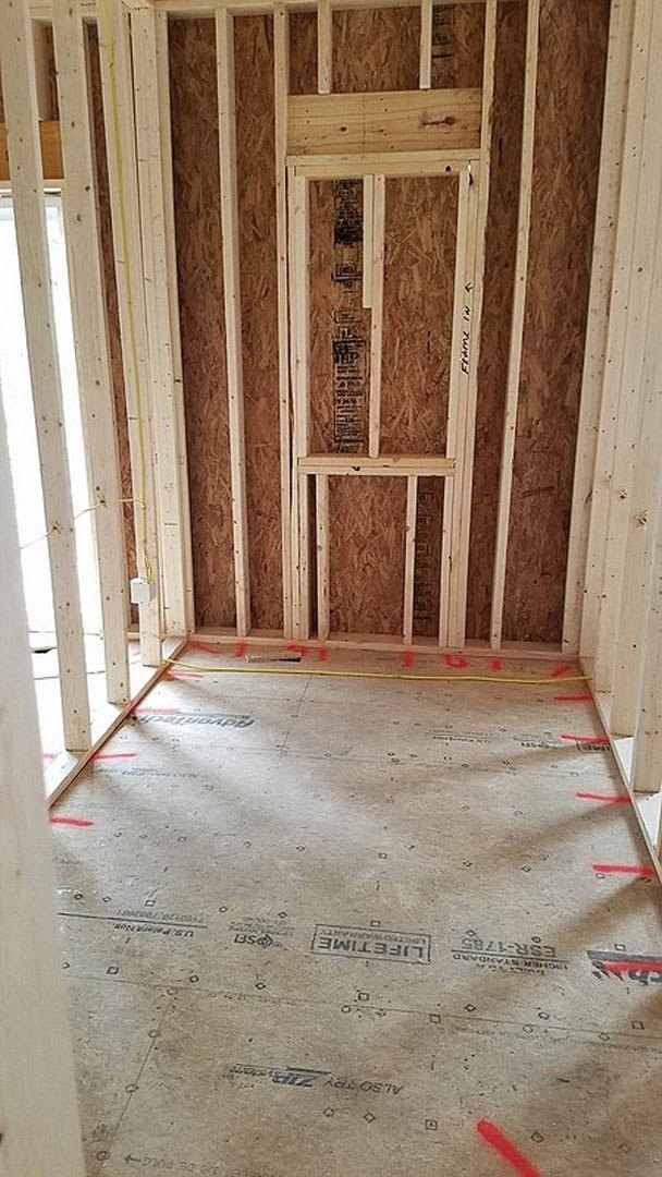 Exposed wood framing and beams in an unfinished interior room with visible insulation and plaster walls