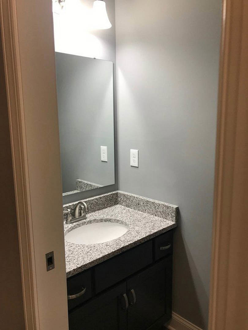 Modern bathroom with rectangular mirror above white countertop, chrome faucet, undermount sink, light gray tile backsplash, and dark wood cabinetry