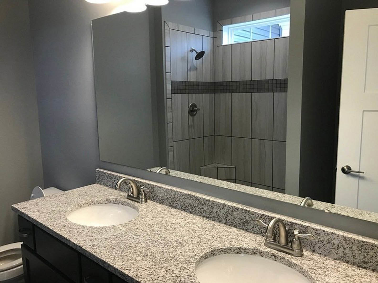 Bathroom featuring granite countertop vanity with undermount sink, glass-enclosed tile shower, chrome fixtures, and light-colored cabinetry