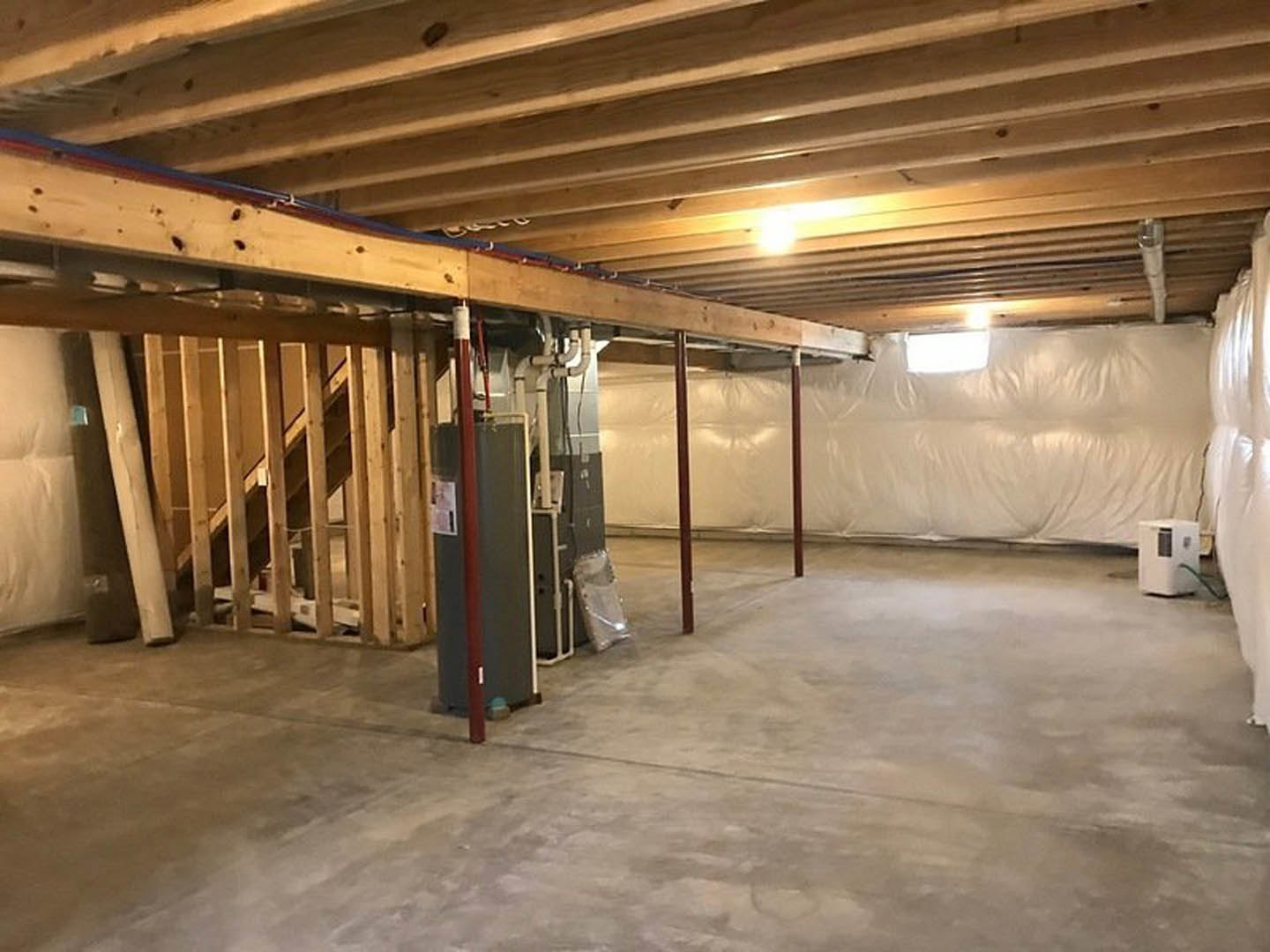 Open room with exposed wood beam ceiling, white plaster wall, concrete floor, recessed ceiling lights, metal support pole, and window in a white box structure.