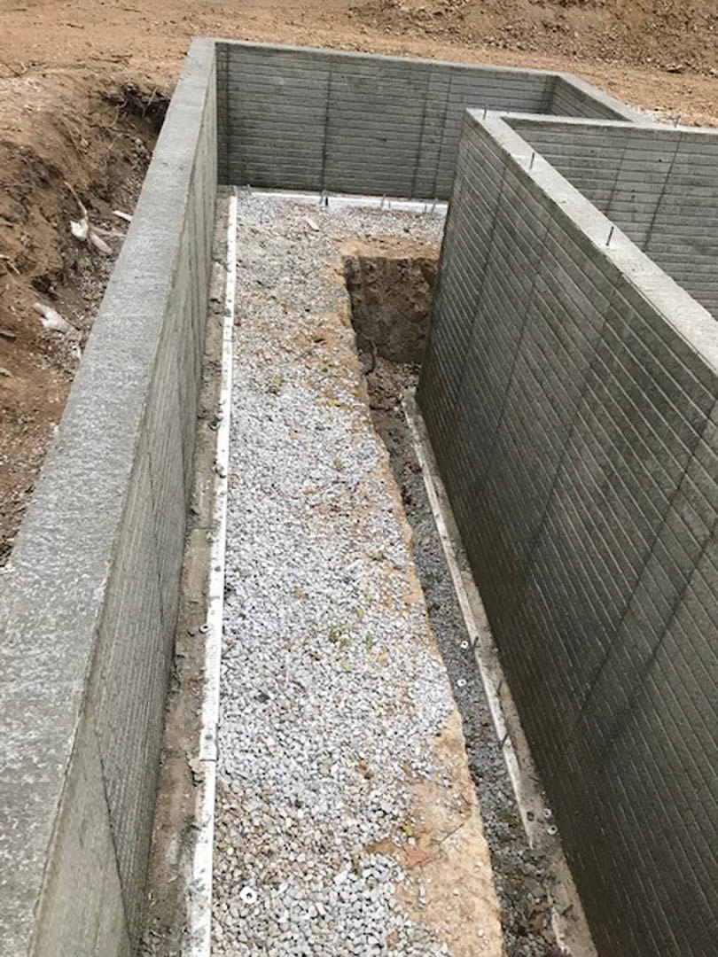 Concrete exterior wall with a circular hole, rough surface texture, exposed aggregate, and surrounding soil at the foundation.