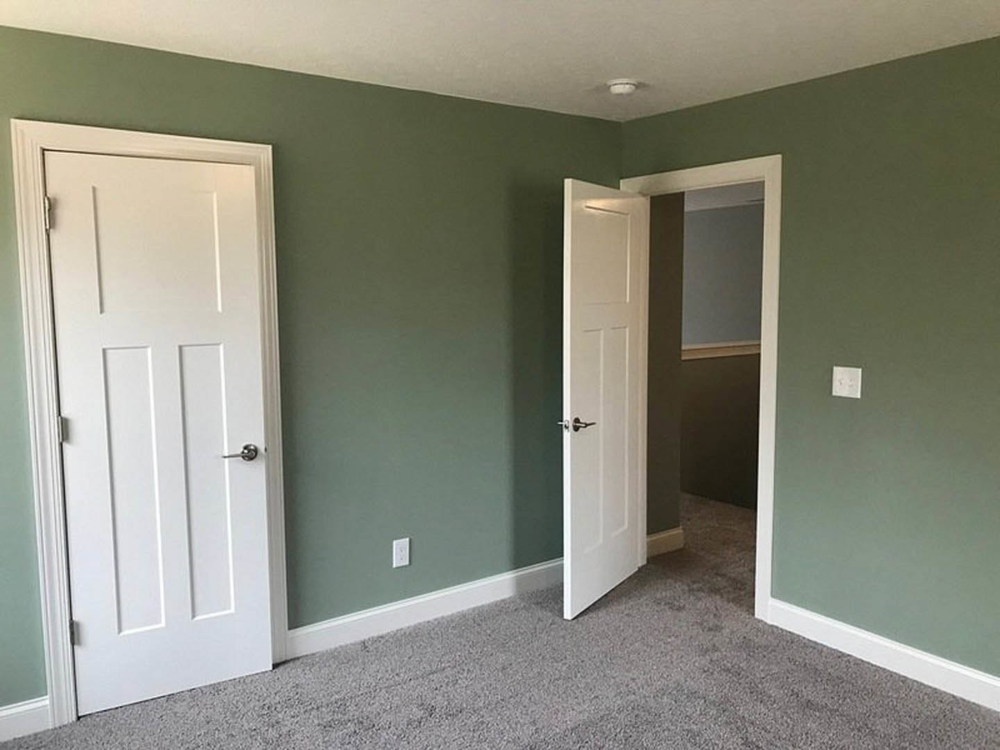 White paneled doors with silver handles set in a room with light wood flooring, white baseboards, and a white square wall feature.