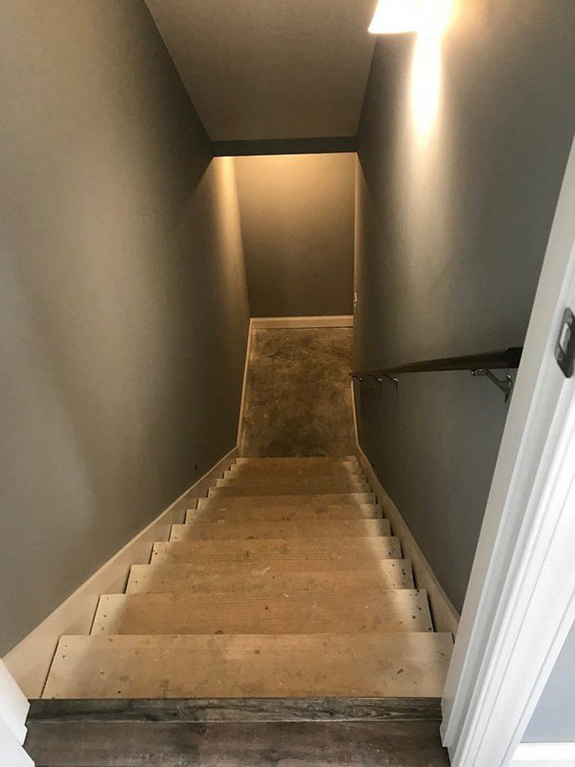Wood and metal staircase with concrete flooring, plaster walls, and hallway above