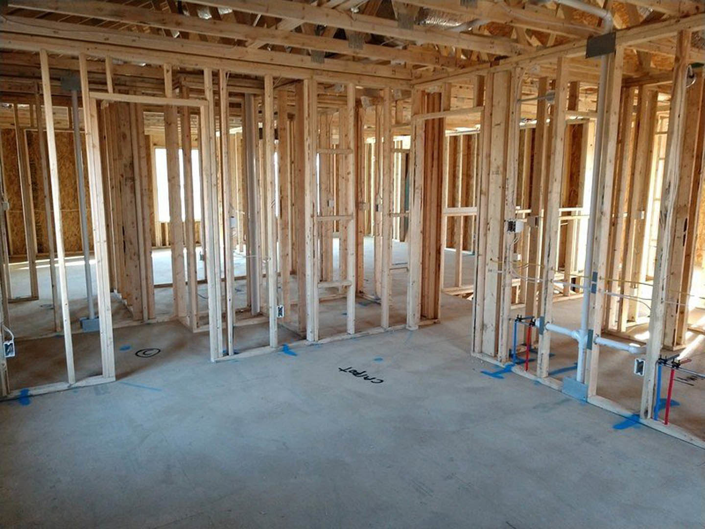 Wood-framed room under construction with exposed beams, concrete floor, building insulation, and a sign featuring black text on a white surface