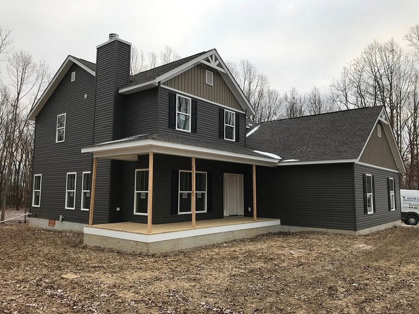 Large unfinished porch with exposed wooden beams, white siding, black-framed windows, and construction materials scattered around the entrance.