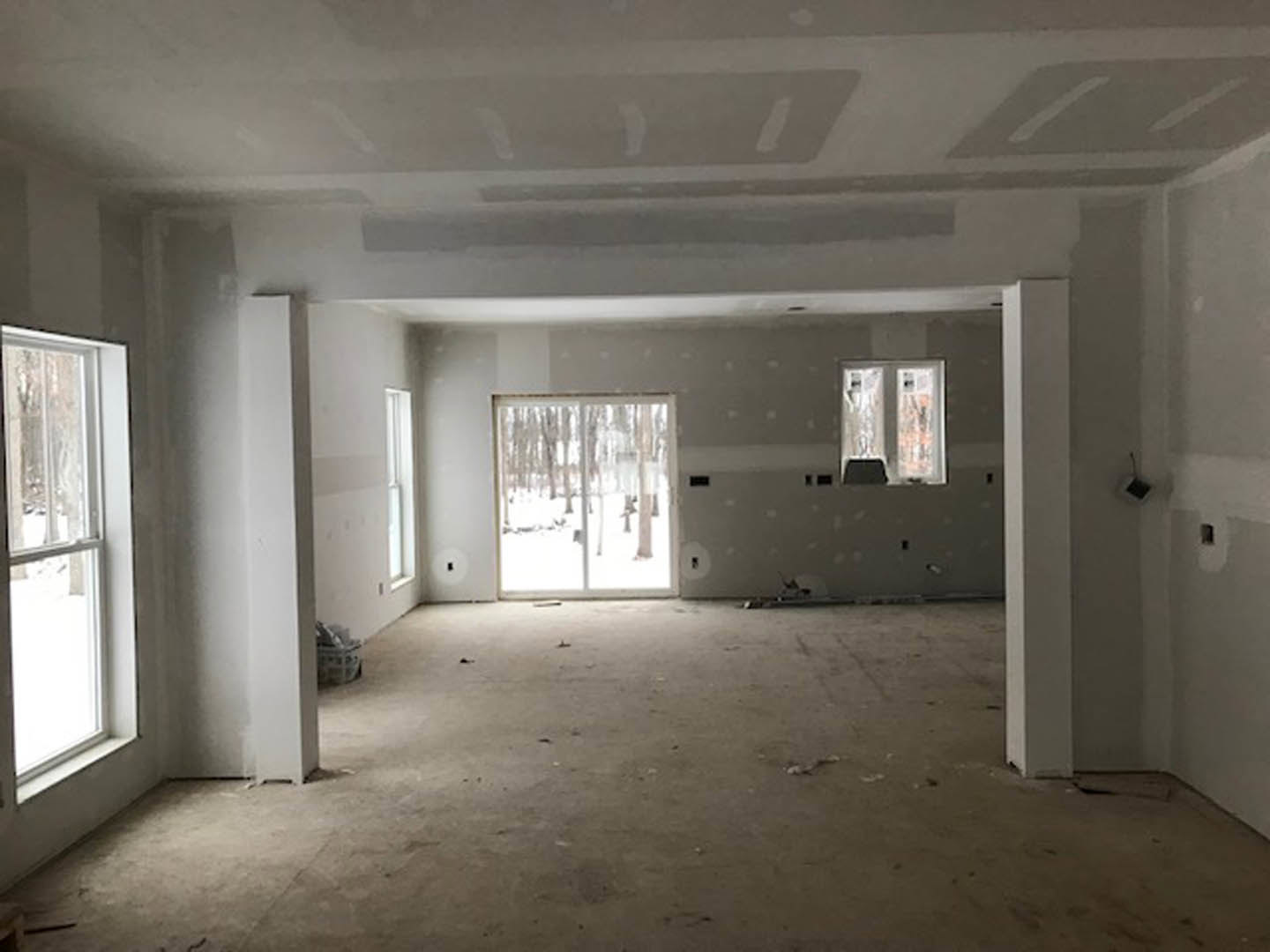 Sliding glass door and large window overlooking snowy forest, light-colored plaster walls, hardwood flooring, woven basket in foreground