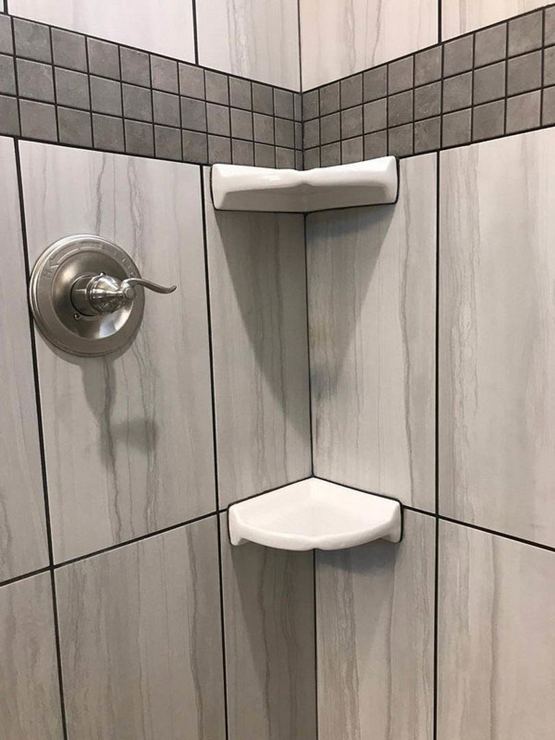 Modern bathroom with white tile walls, dual shower heads, black-trimmed corner sink, built-in shower shelf, chrome bathtub handle, and close-up of white wall detailing