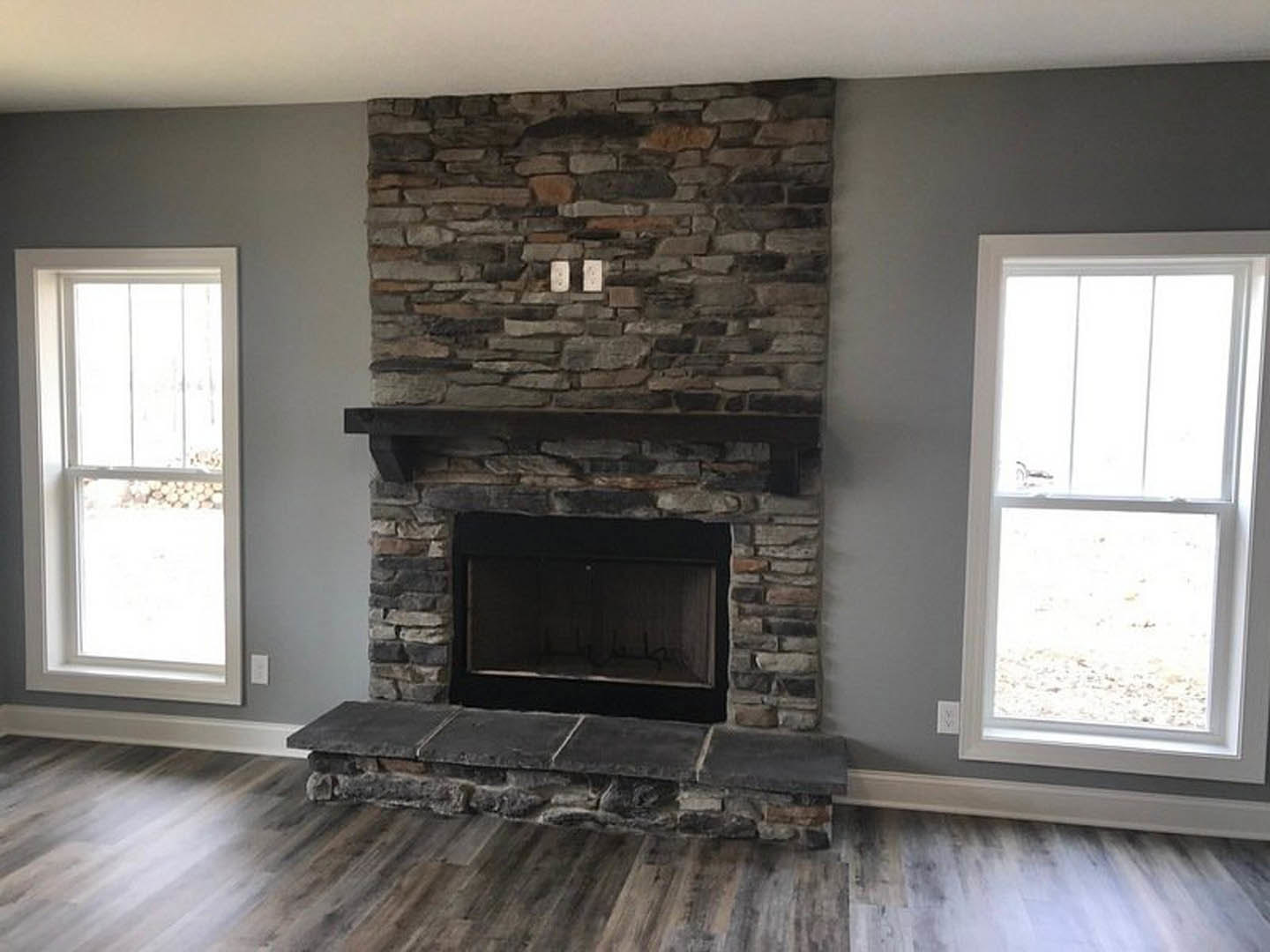 Stone fireplace with black frame and wood mantel, stone hearth on light wood floor, white-framed window on adjacent wall