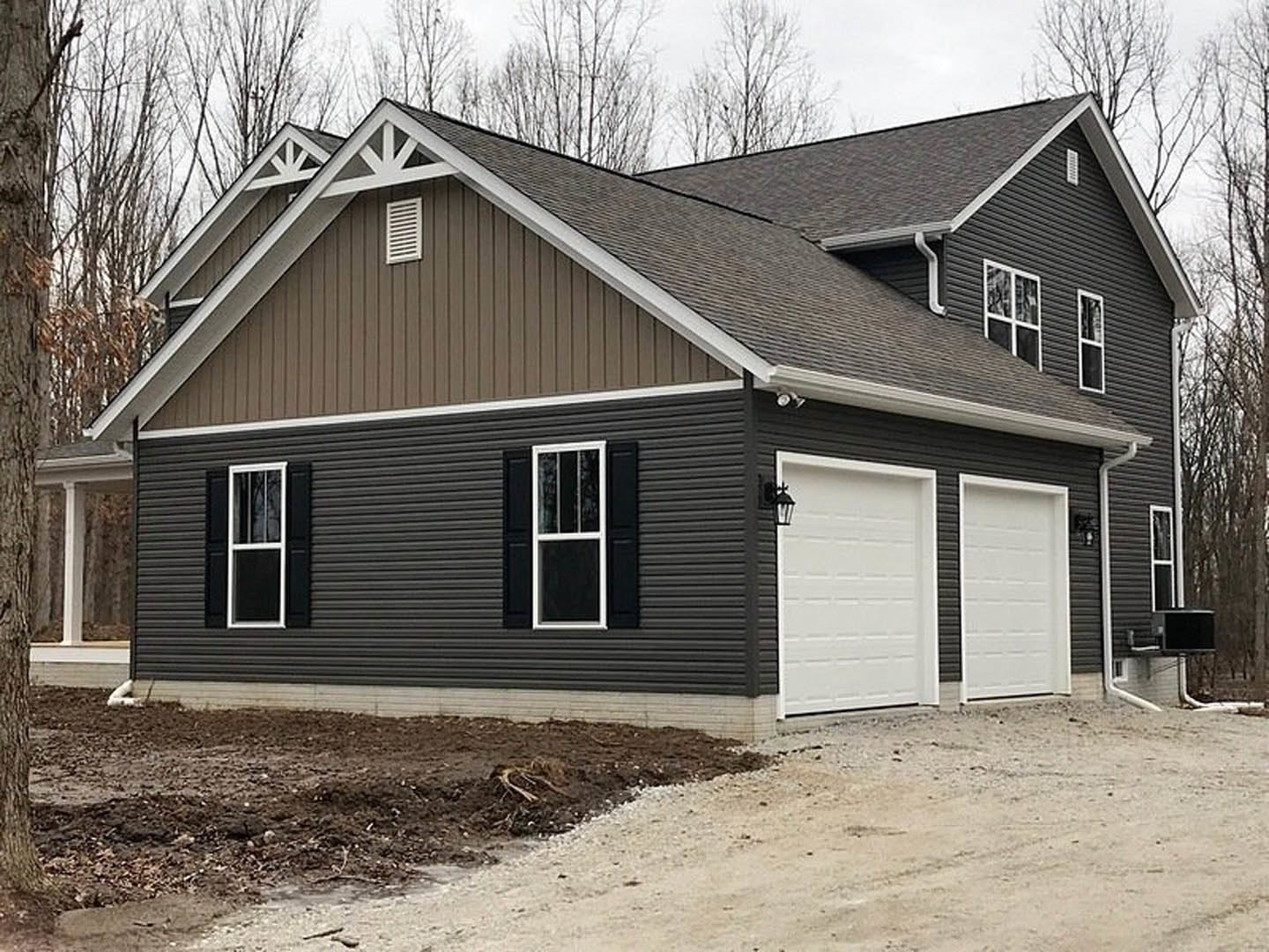 White two-story house with black trim, white garage door with exterior lamp, white-framed window, vent on wall, tree in front yard, blue sky overhead.