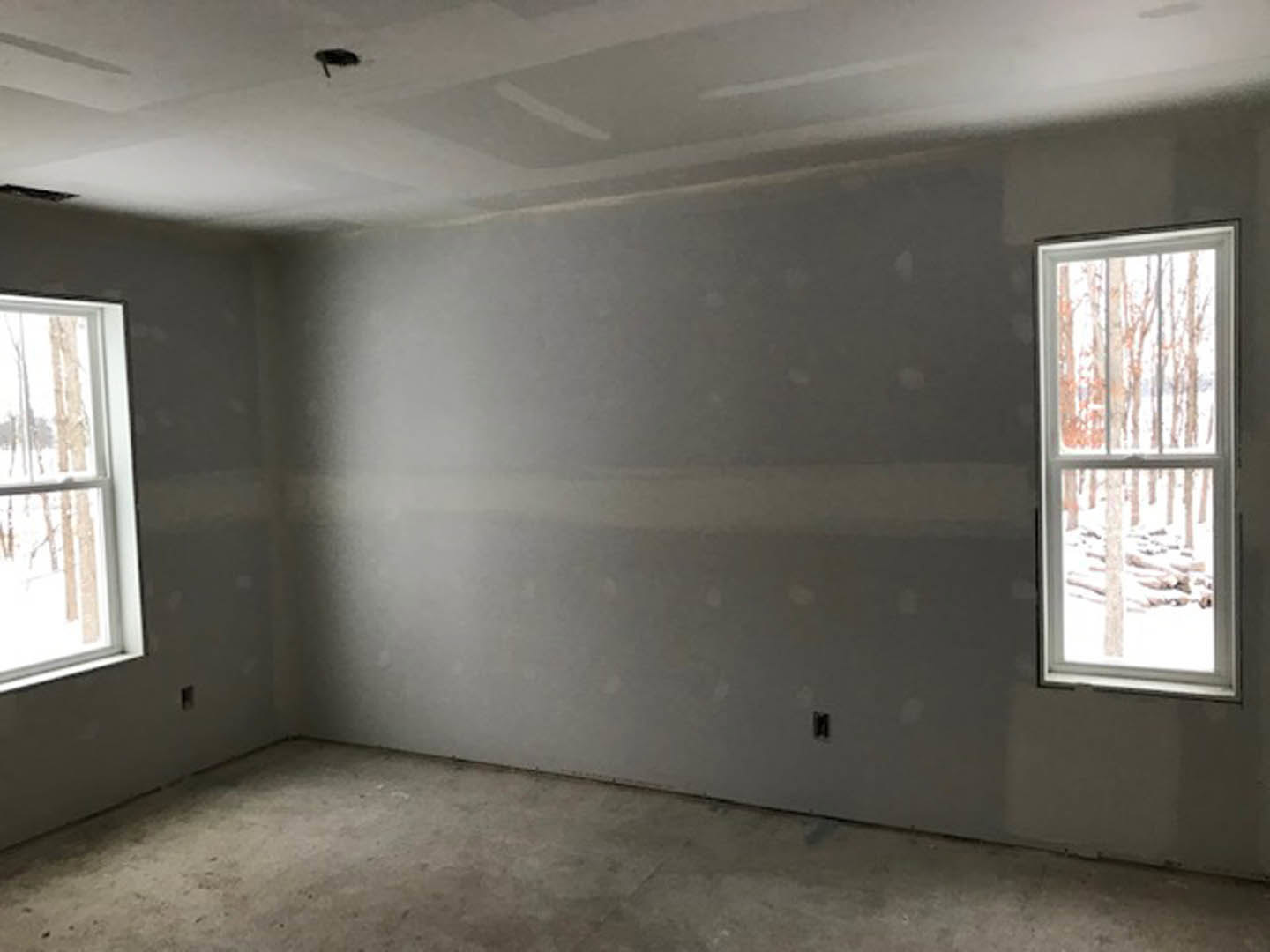 Bright room with white plaster walls, large window overlooking snowy trees, smooth concrete floor, white ceiling with recessed light fixture