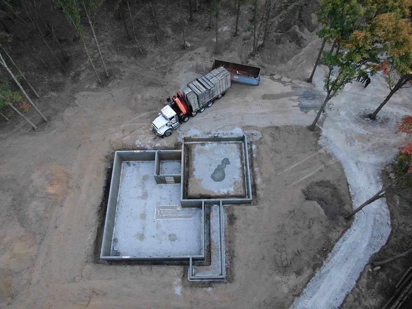 White pickup truck parked beside a modern home with concrete foundation, surrounded by bare trees and wet ground.