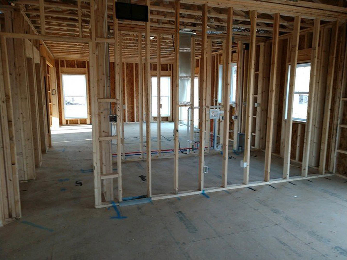Wood-framed room under construction with exposed beams, window overlooking snowy landscape, wooden ceiling, metal bin, and black rectangular object on unfinished floor