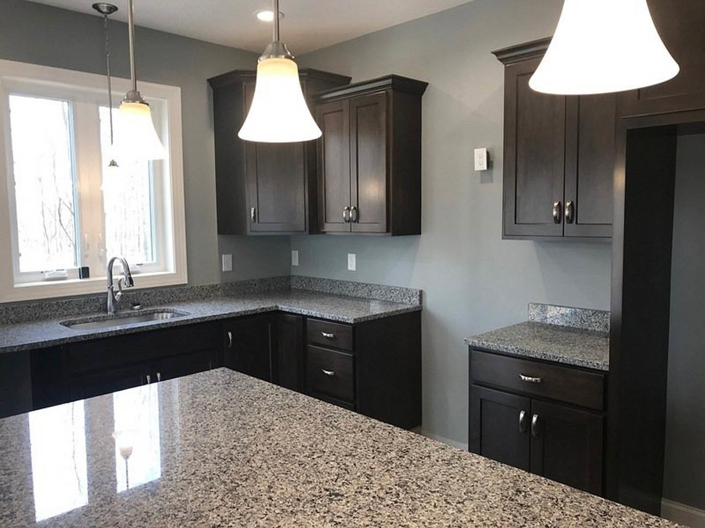 Granite countertops, tile backsplash, white cabinetry, stainless steel sink beneath ceiling light fixture, black drawer on kitchen island