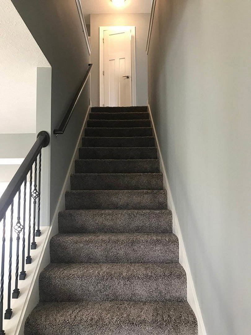 Carpeted staircase with white wooden railing, grey carpet, and adjacent white door illuminated by overhead light